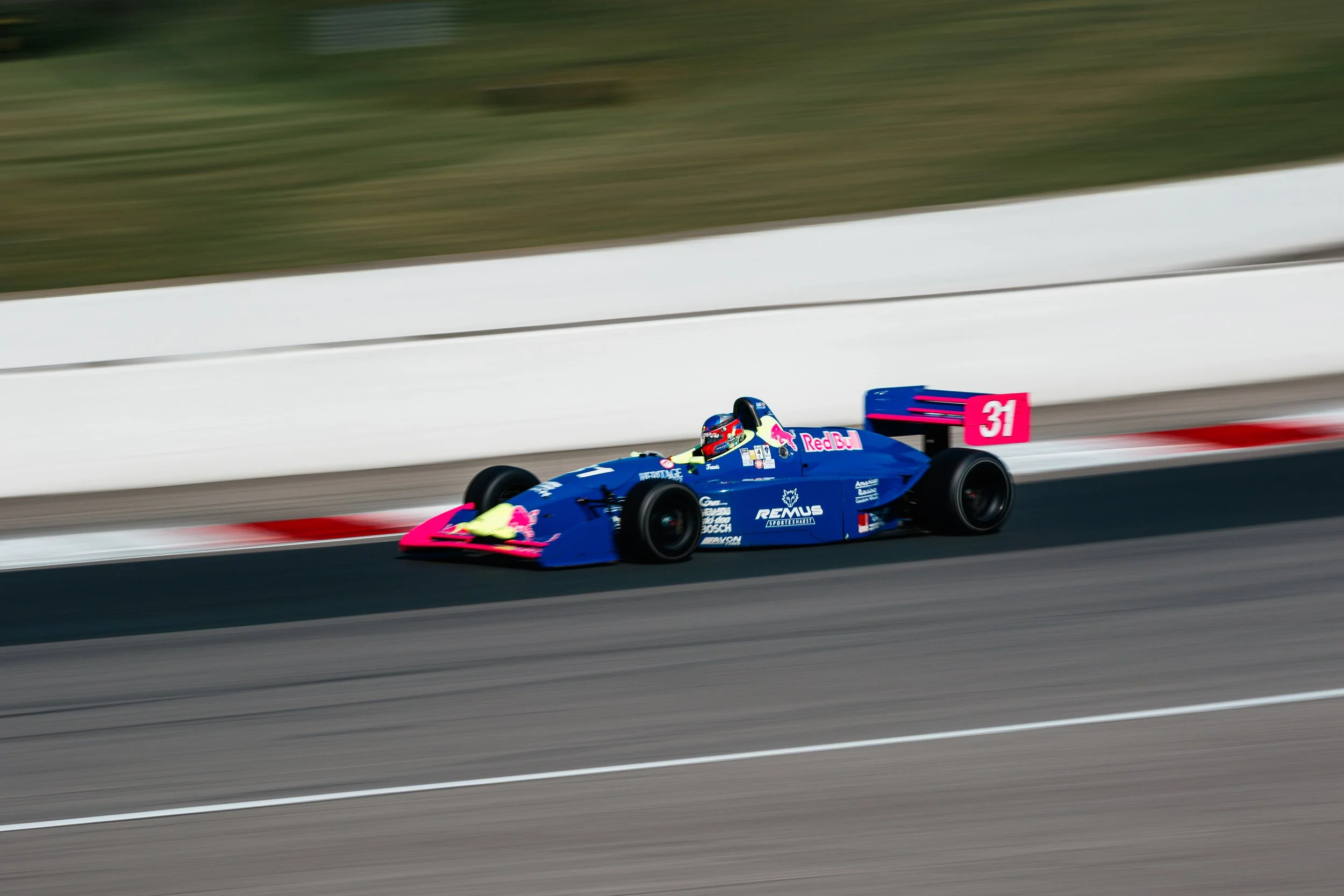 A blue race car with pink accents, number 31, on a race track, moving at high speed.
