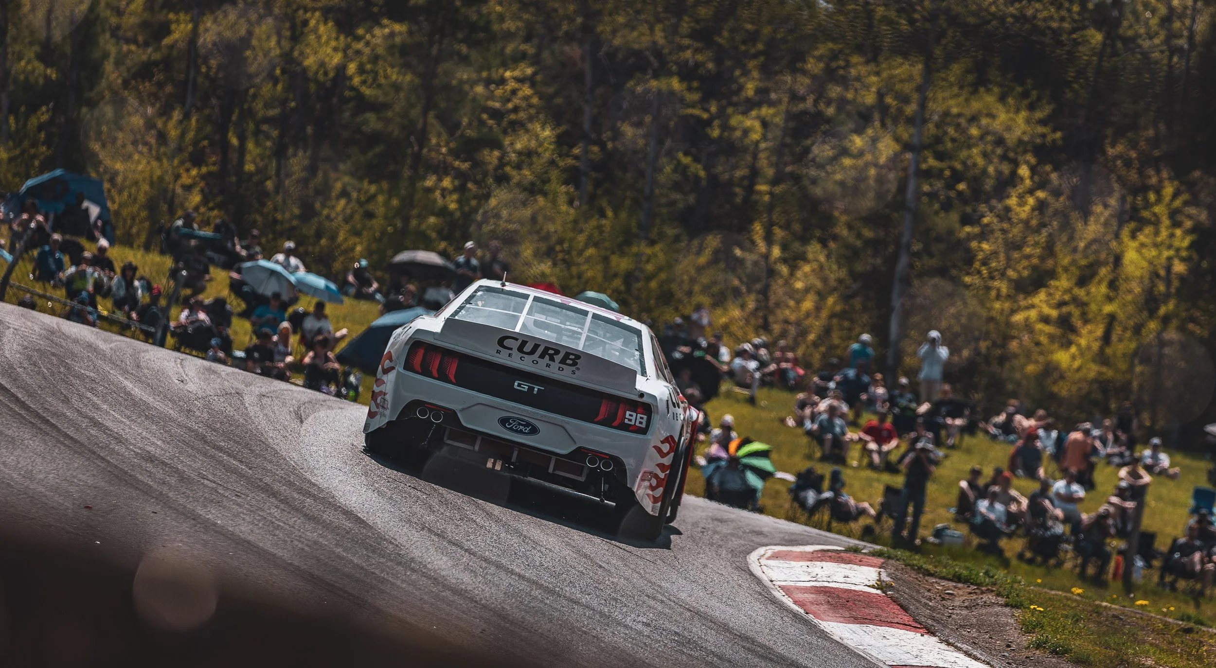 Race car on a racetrack with spectators watching from a grassy hillside.