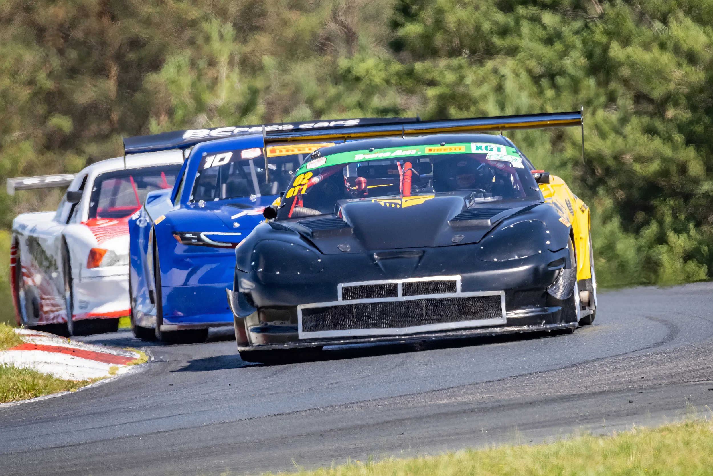 Race cars on a track during a race, with a forested background.