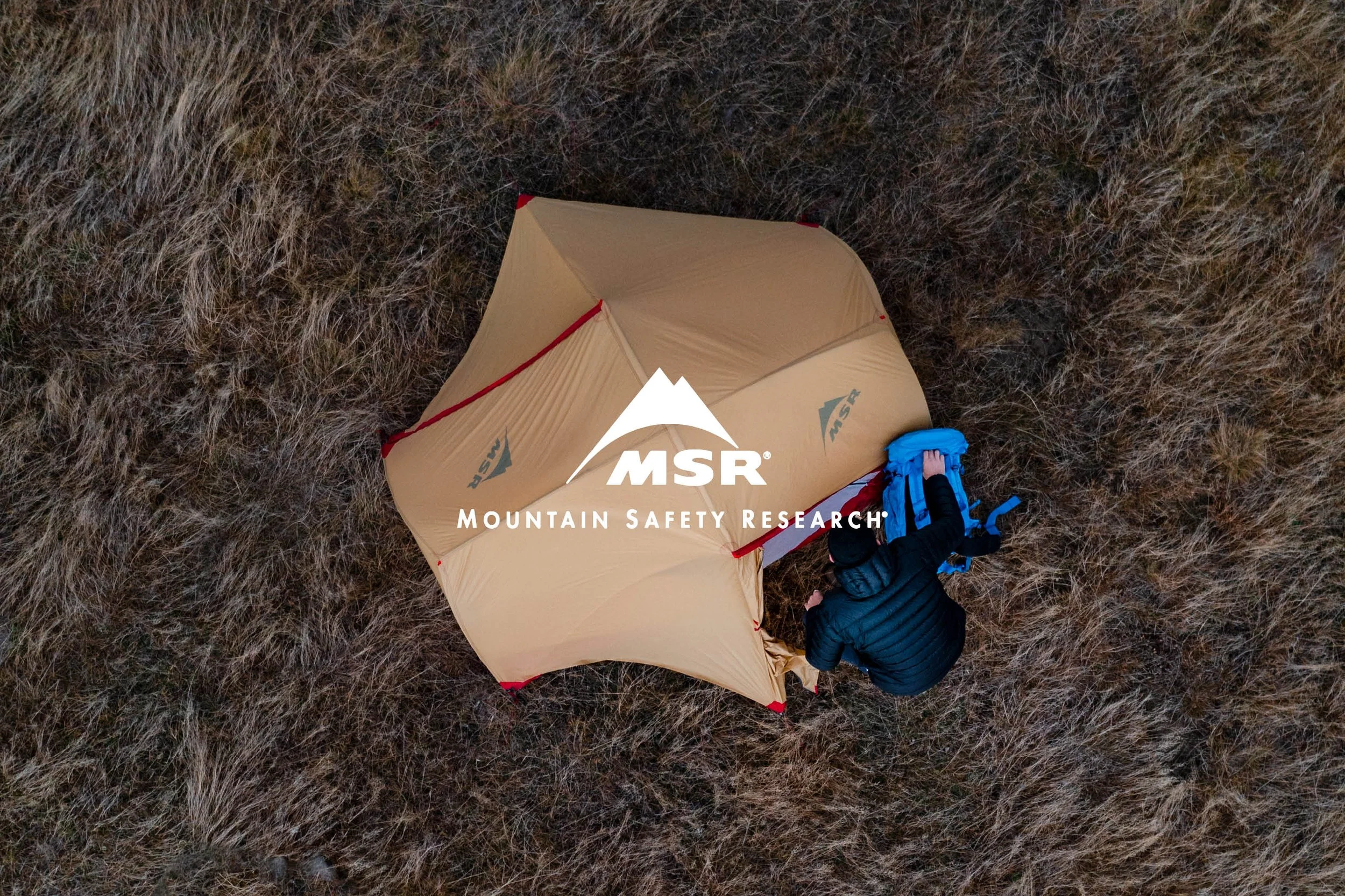 Overhead view of a person setting up a tan MSR tent in a grassy area.