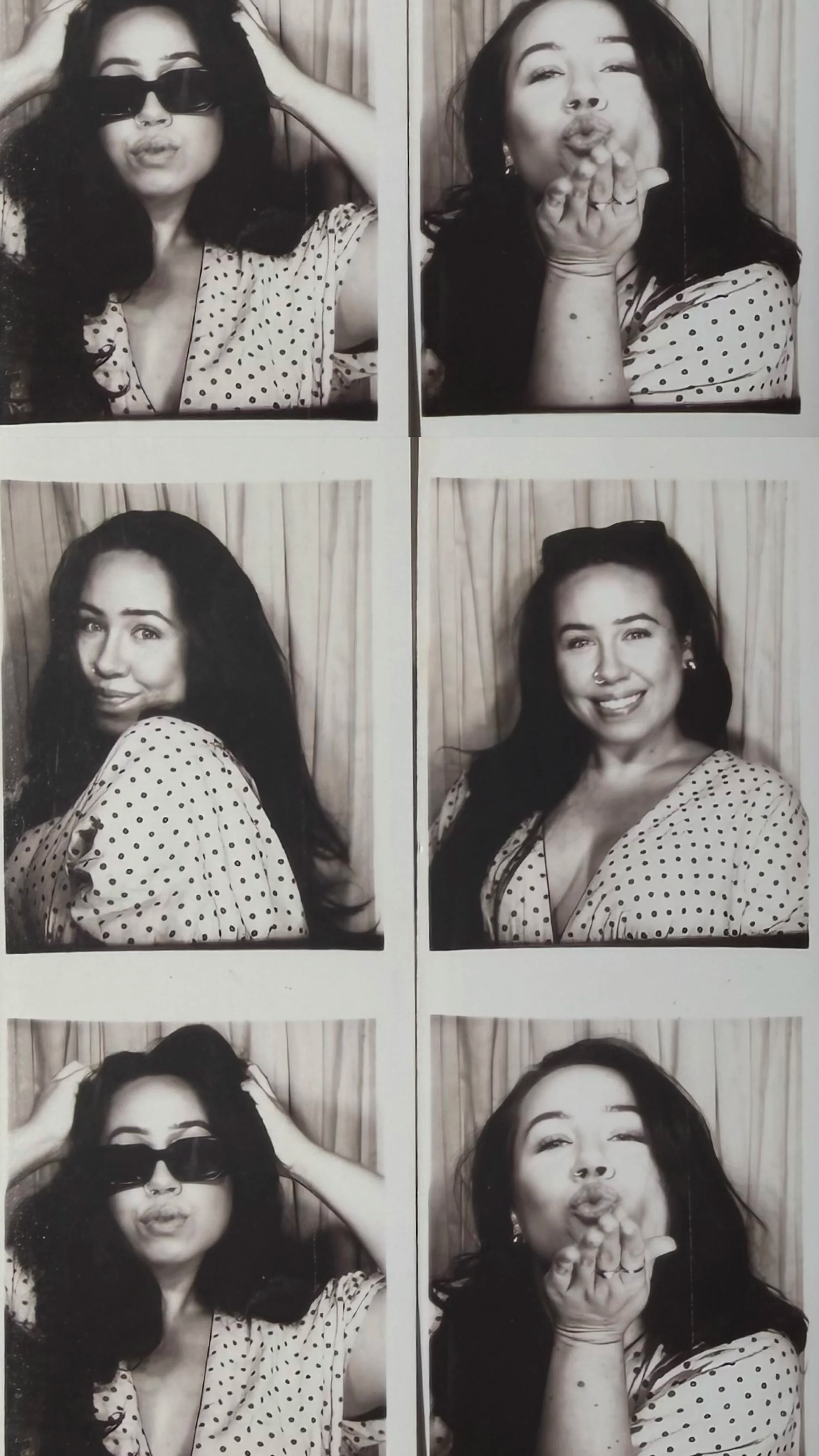 A photo booth strip with four black and white pictures of a woman with long dark hair wearing a polka dot dress. In the first photo, she wears sunglasses with her hands in her hair. In the second, she blows a kiss towards the camera. In the third, she looks over her shoulder with a slight smile. In the fourth, she holds her hands to her glasses and pouts.