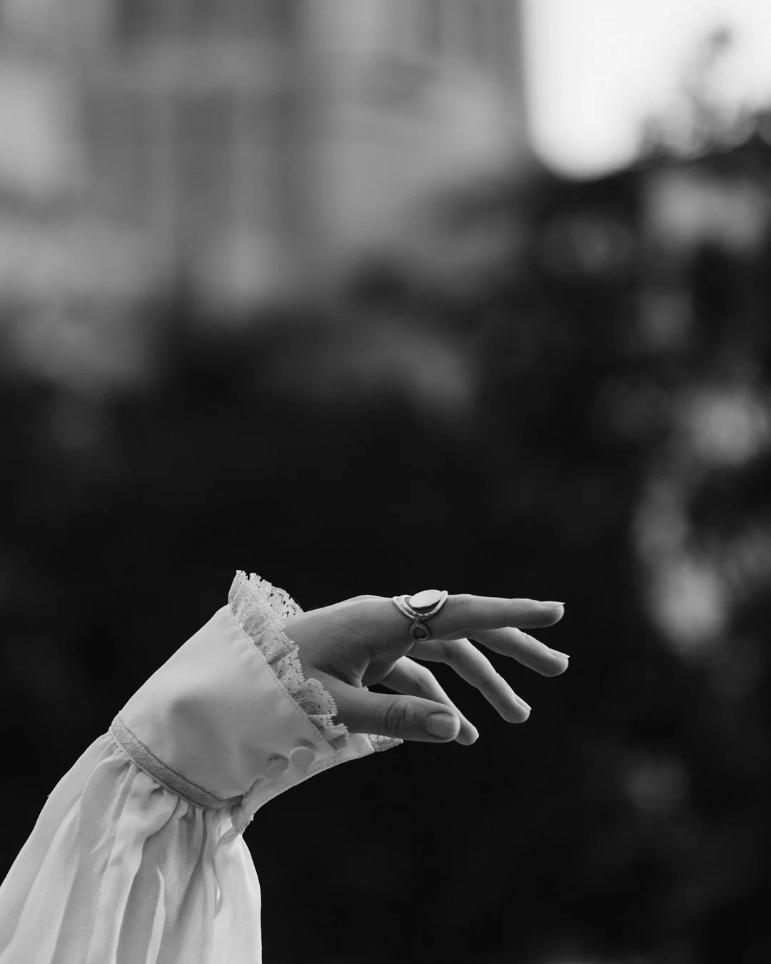 A black and white photo of a right hand extended with fingers slightly spread, wearing rings and a sleeve with lace trim.