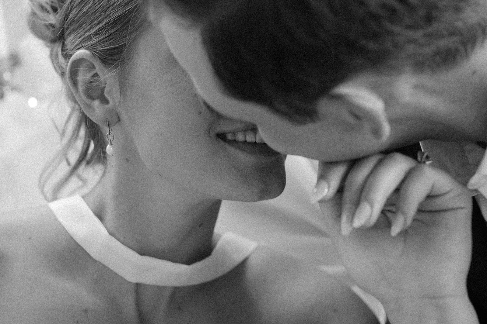 Close-up of a couple about to kiss, with the woman's face turned slightly away from the camera and smiling, and the man's face close to hers. The woman has a pearl earring and earrings, and the man has short hair. Black and white photo.