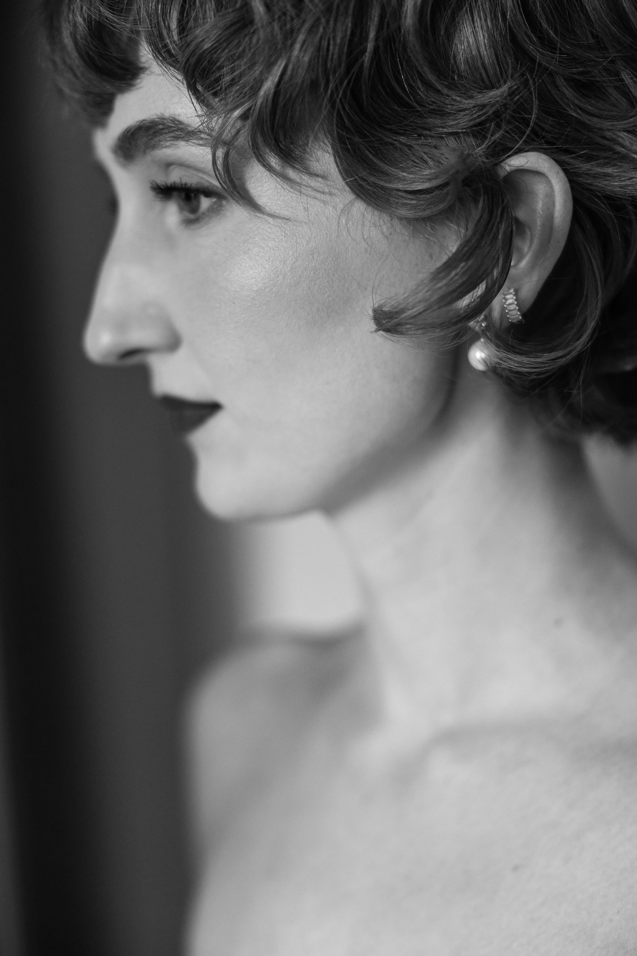 Close-up black and white photo of a woman's face in profile with curly hair, wearing earrings.