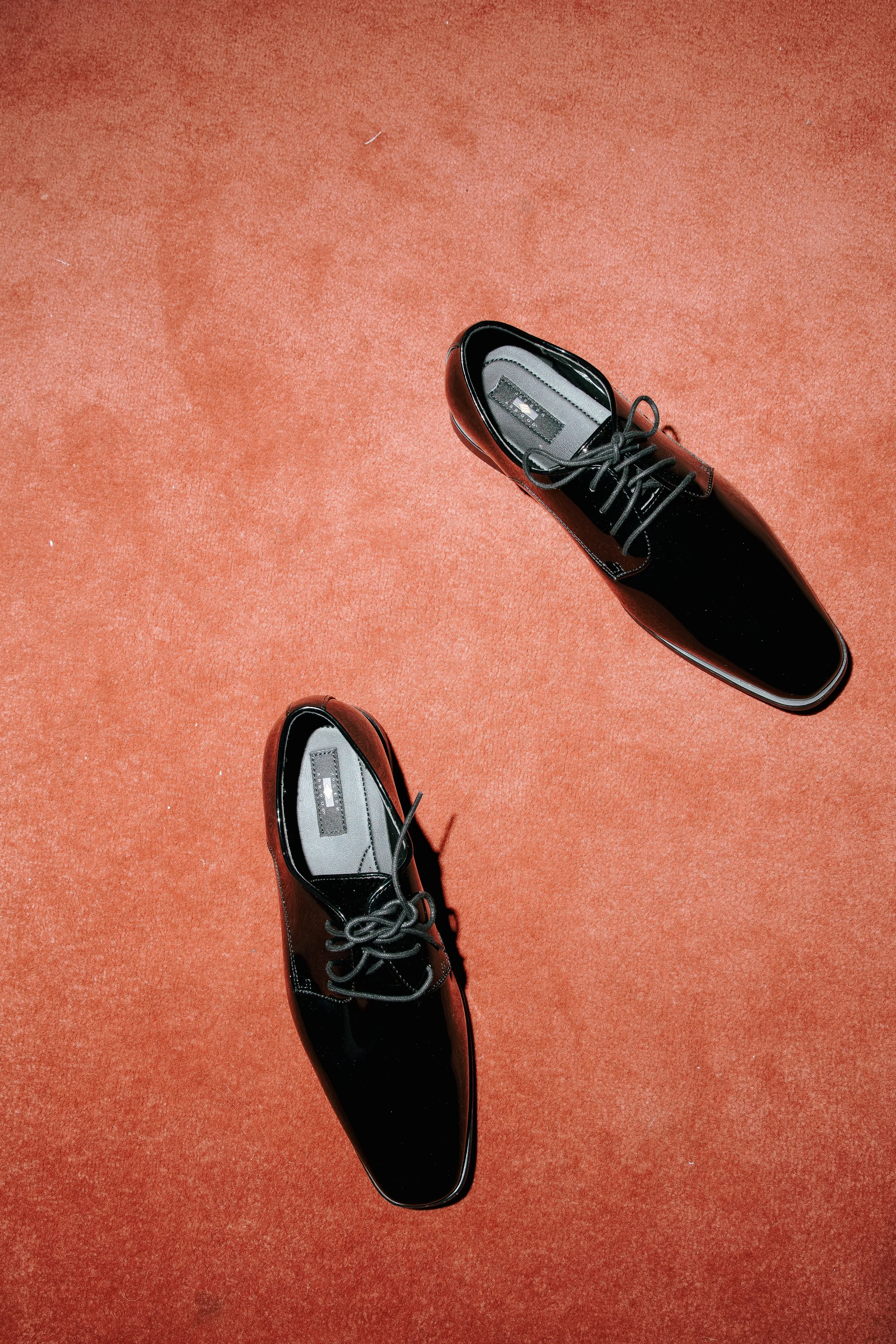 Black shiny lace-up shoes on a red surface.