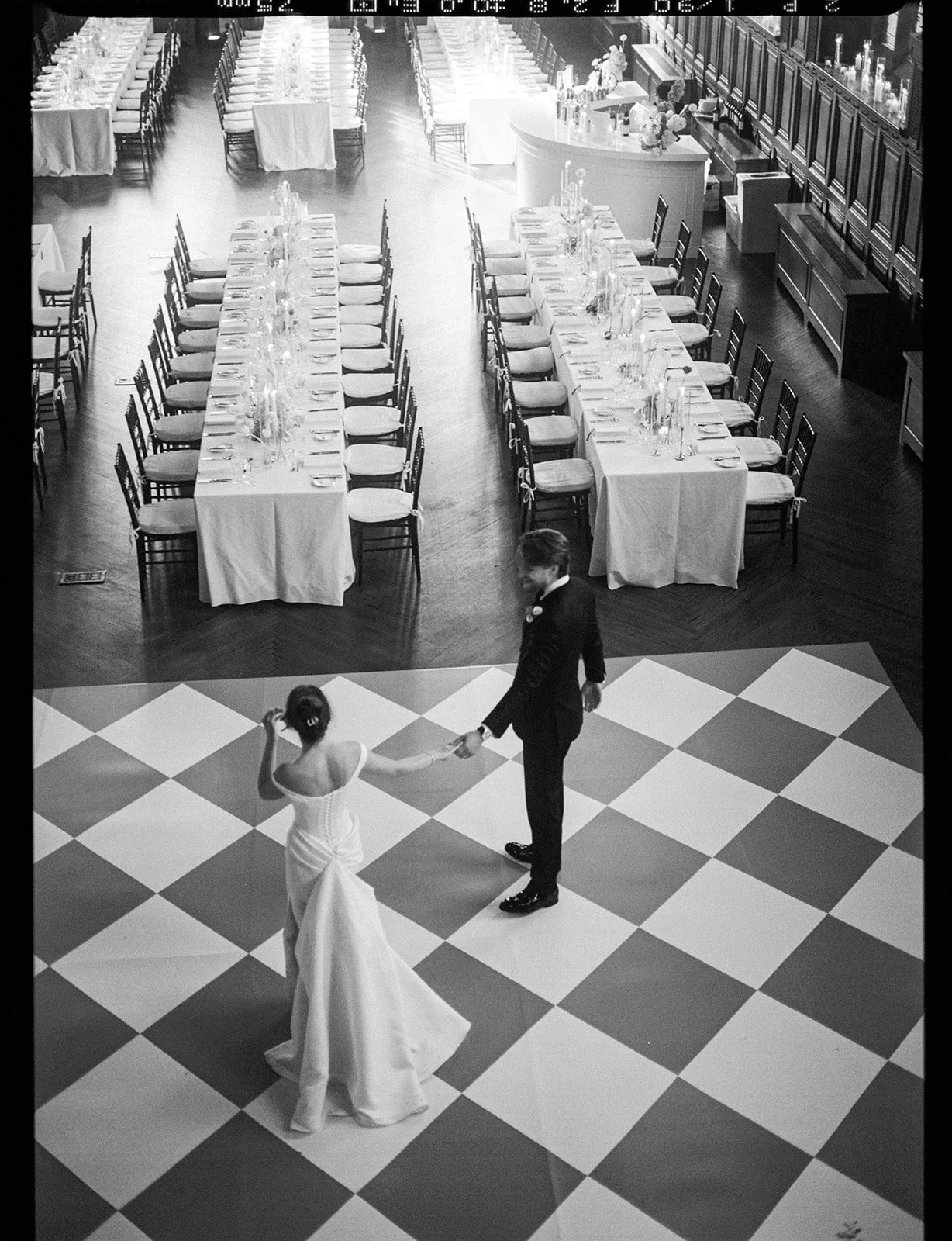 A bride and groom dancing on a checkered dance floor at their wedding reception, with tables set up in the background for guests.