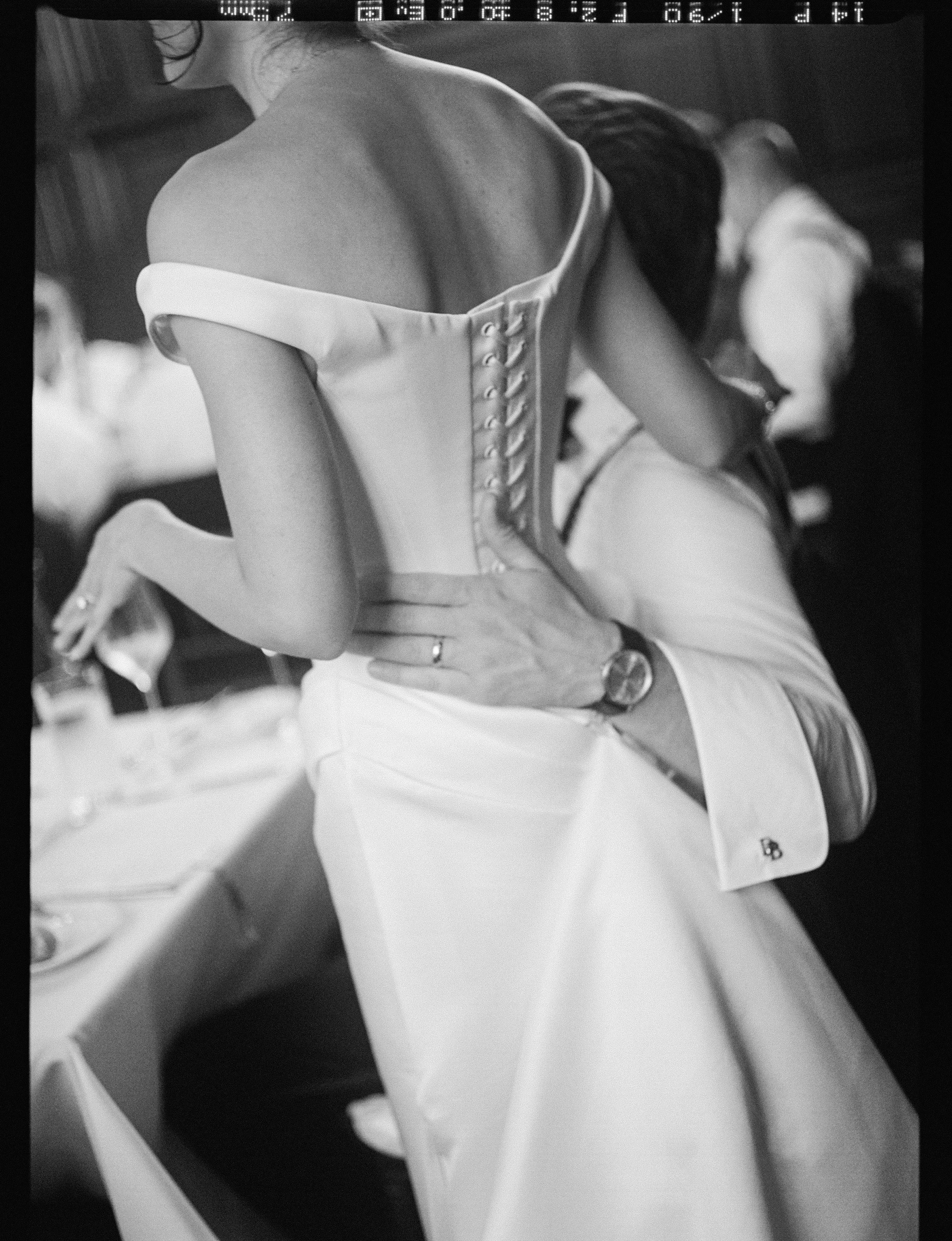 A woman in a white dress sitting on a bed, with her head turned down and hair covering her face.