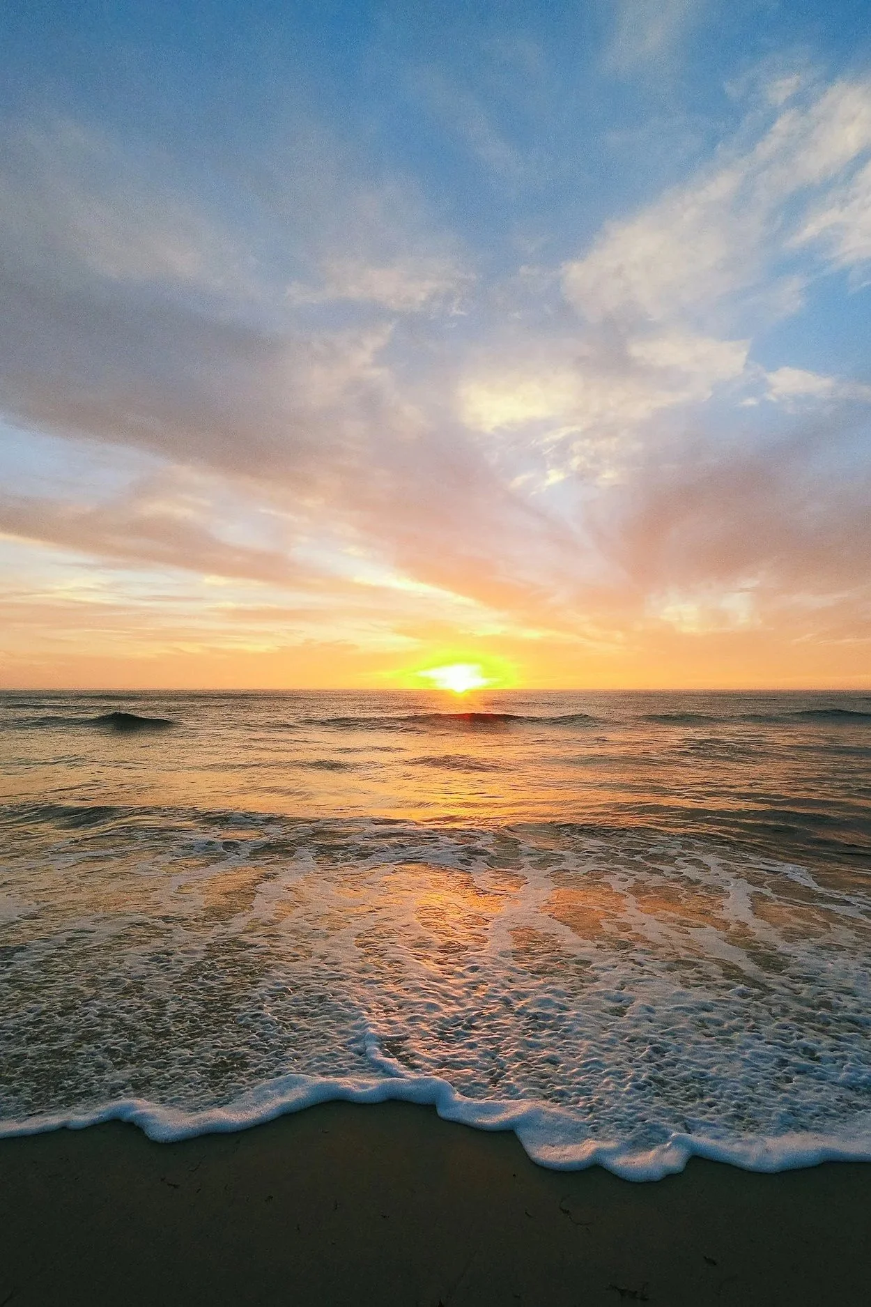 Sunset over calm ocean waves with a partly cloudy sky.