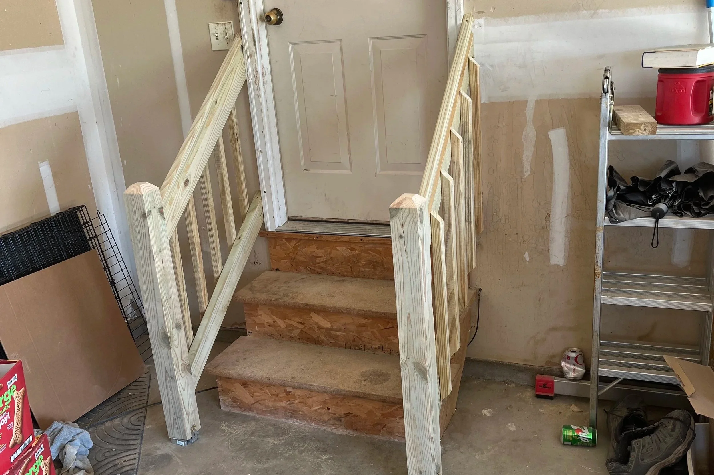 Interior of a garage with a new wooden staircase leading to a door, surrounded by construction materials and tools.
