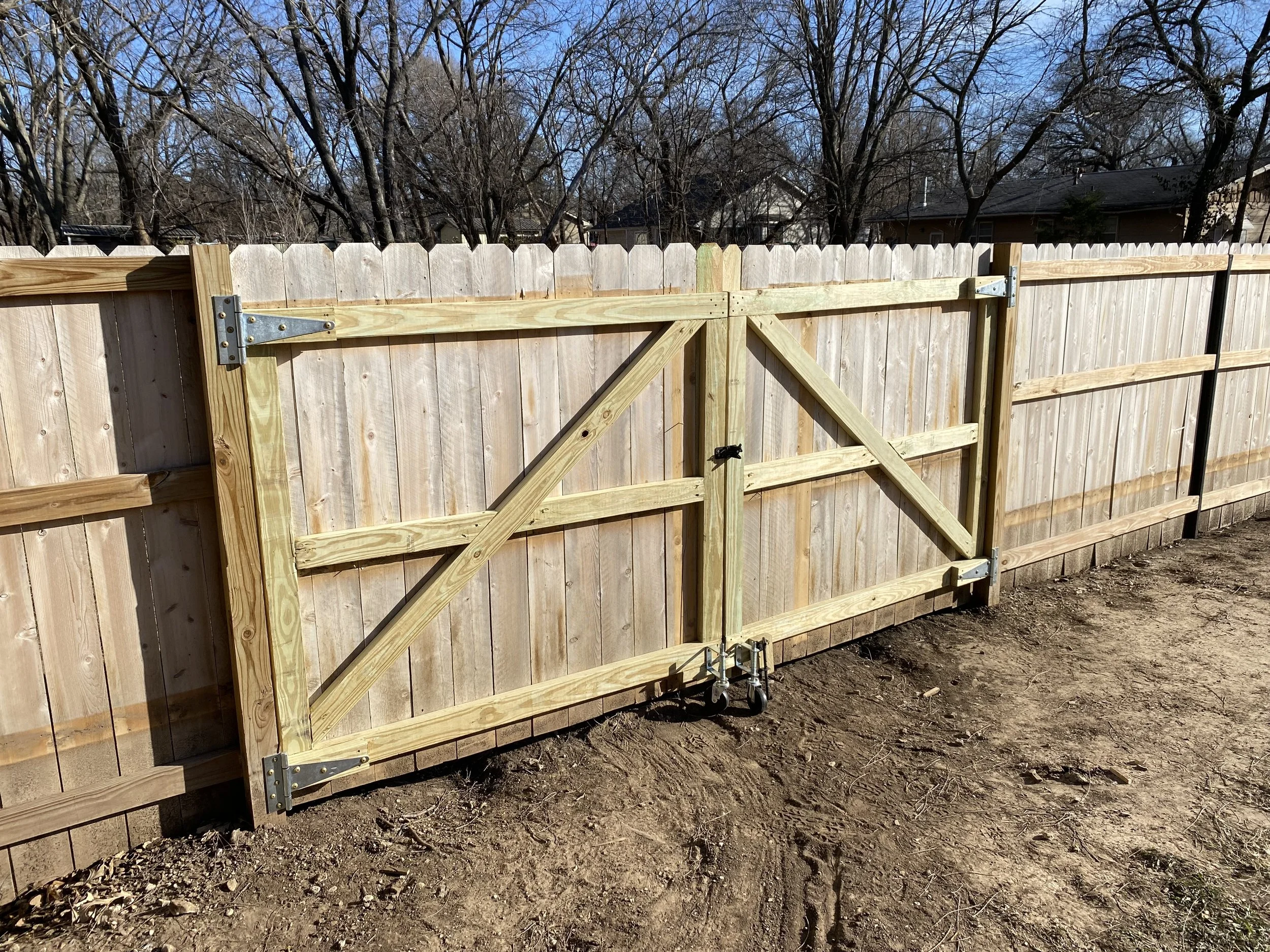 A wooden fence with a gate, trees in the background, and a house roof visible on the right side.