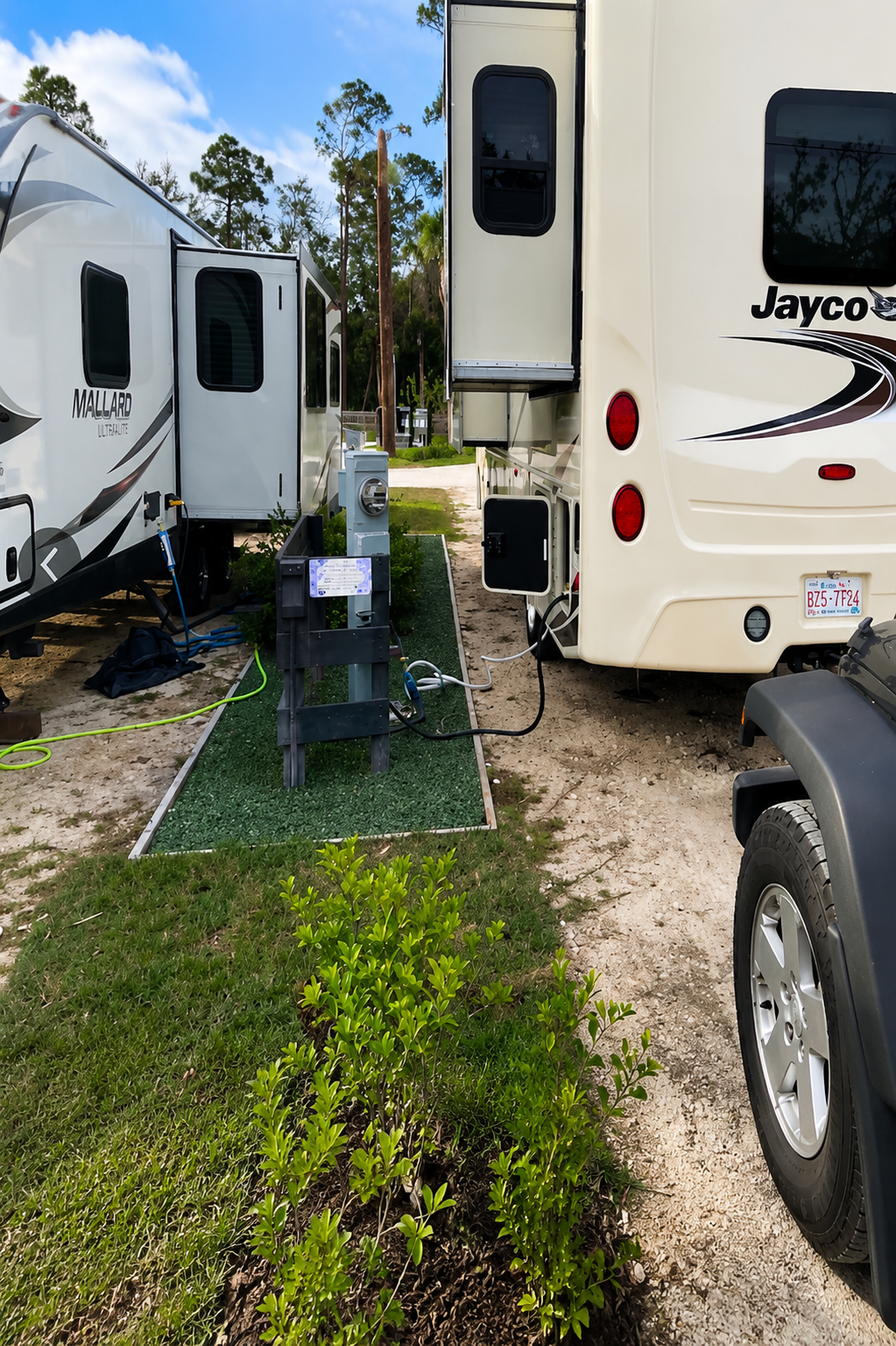 Two RVs parked side by side with electrical hookup on a grassy area at a campground.