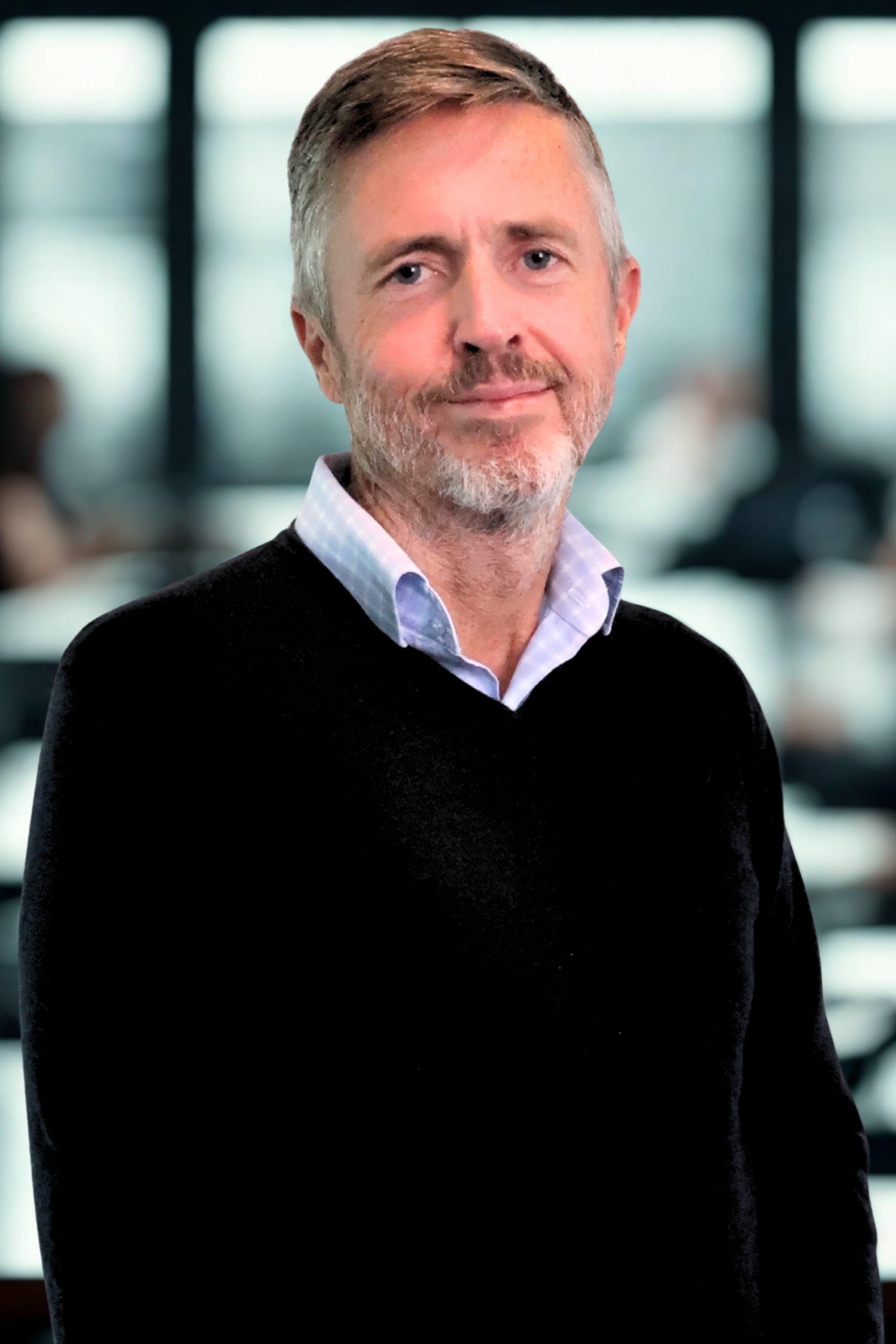 A middle-aged man with a gray beard and short, light brown hair, wearing a black sweater over a collared shirt, smiling slightly, in an indoor office setting with blurred background.