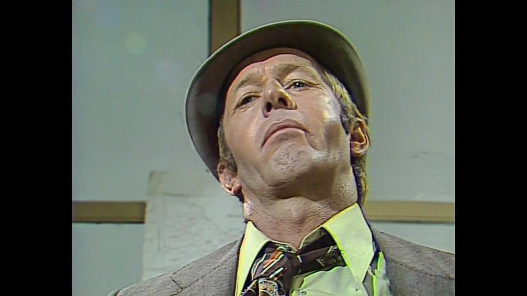 A man wearing a hat, with a serious expression, looking down at the camera.