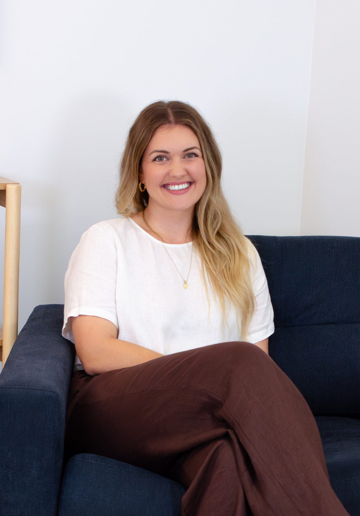 Smiling woman with a white shirt and brown pants sitting in an armchair