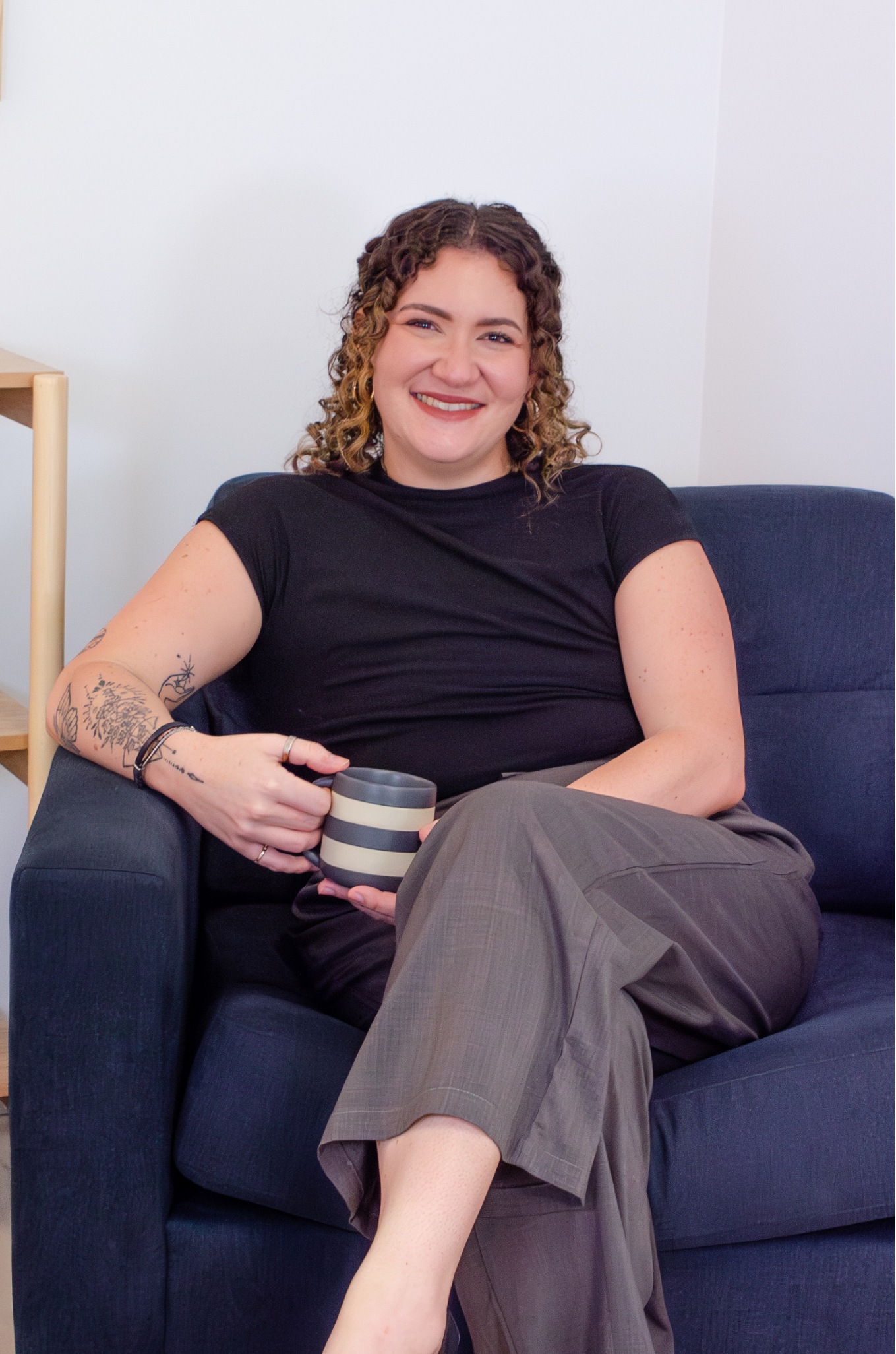 Smiling woman in a black blouse sitting on a navy blue armchair holding a mug