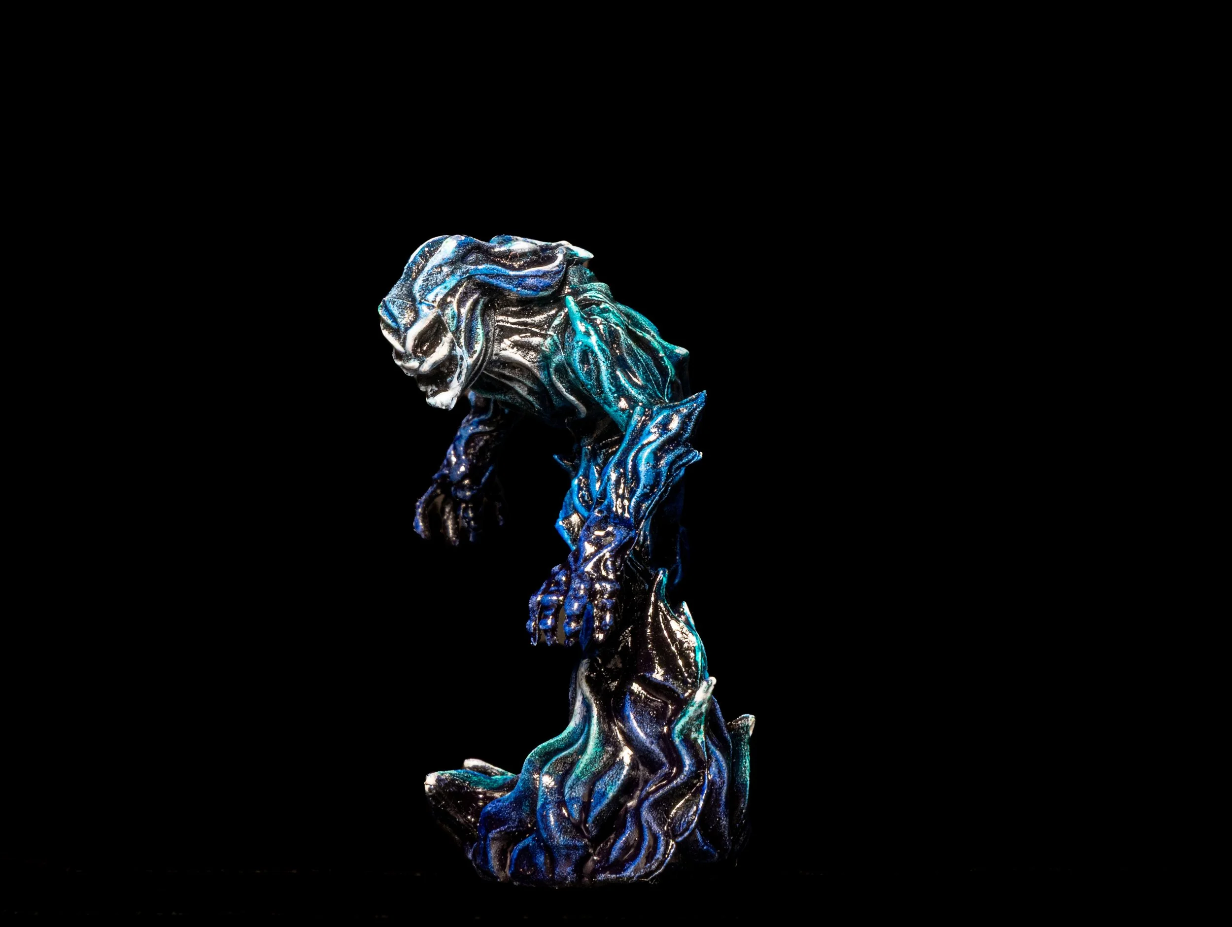 A shiny, abstract sculpture resembling a crumpled piece of paper or fabric, made of metallic material with blue, silver, and black colors, set against a black background.