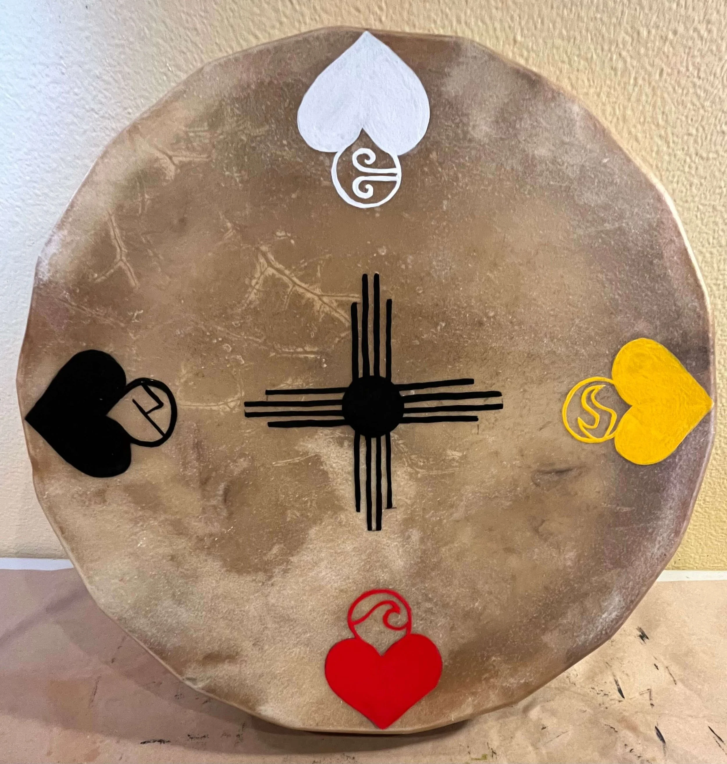 Decorative drum top with various painted symbols, with some black and yellow accents.