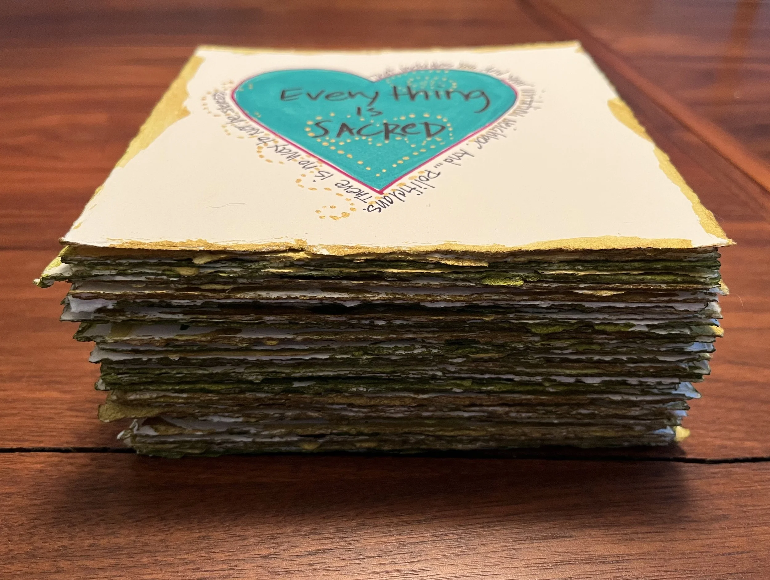 A stack of handmade paper with a colorful heart design on the top sheet that says "Everything is Sacked".
