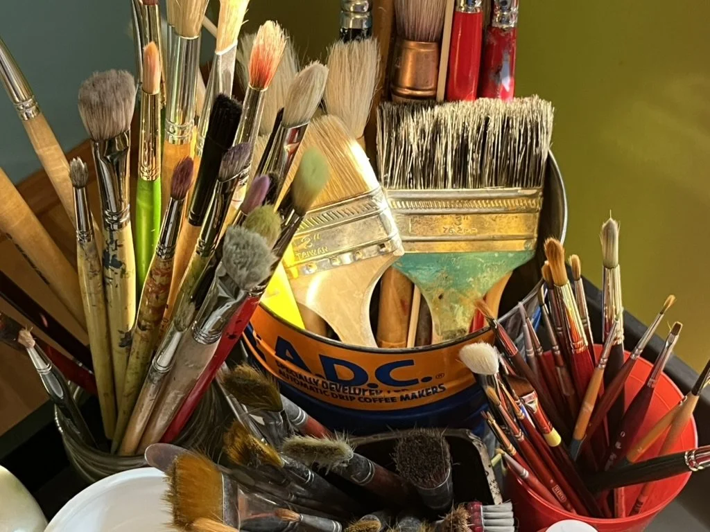 Collection of various paintbrushes in cups on a colorful background.