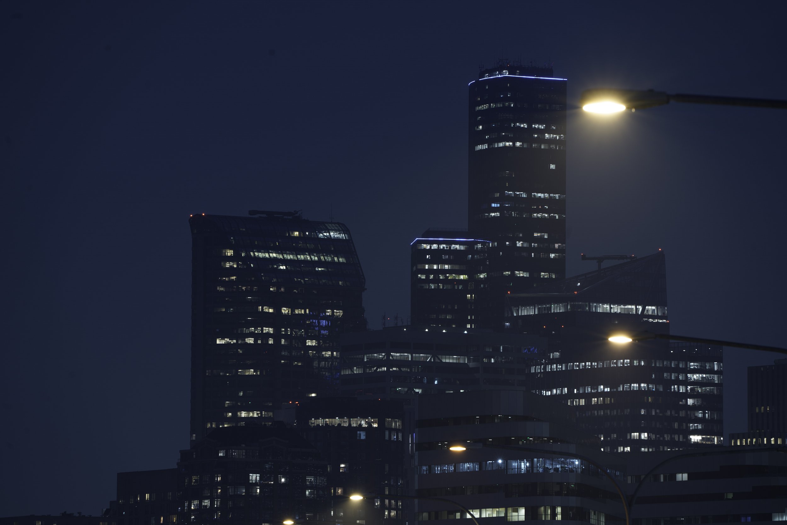 Night view of tall modern skyscrapers in an urban city, illuminated windows and streetlights, dark sky.