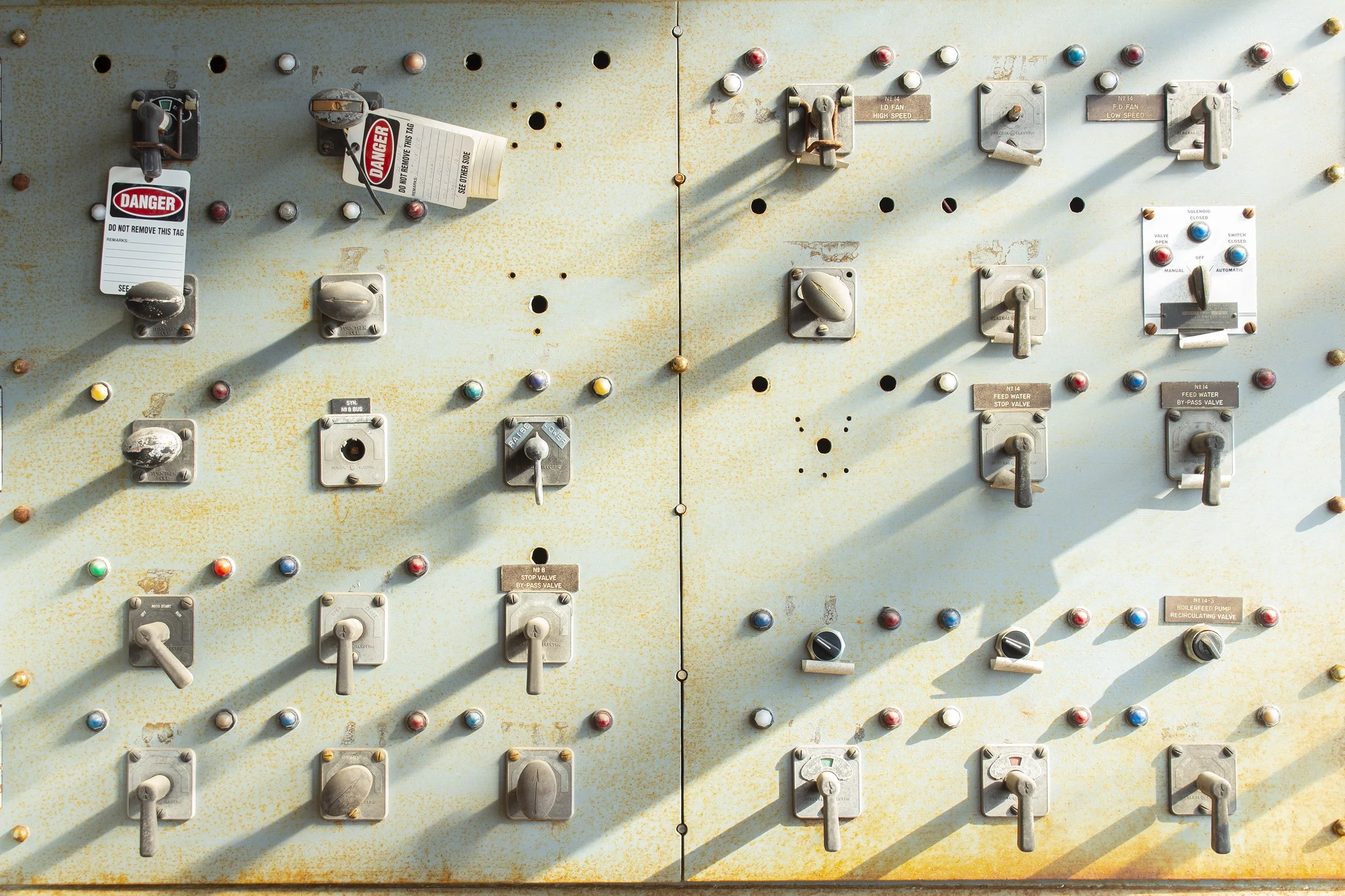 Close-up of an old, weathered electrical control panel with various switches, buttons, and labels, some with warning tags and rusted parts.