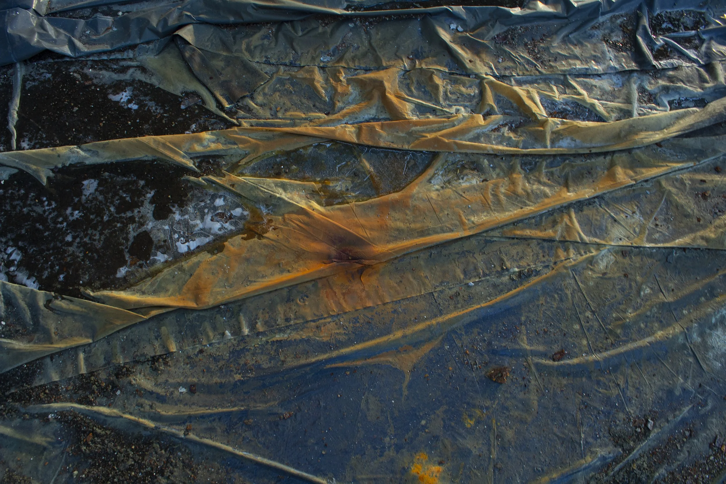 Close-up of a plastic sheet or tarp that is wrinkled and partially covered with dirt and debris, possibly on a muddy ground.