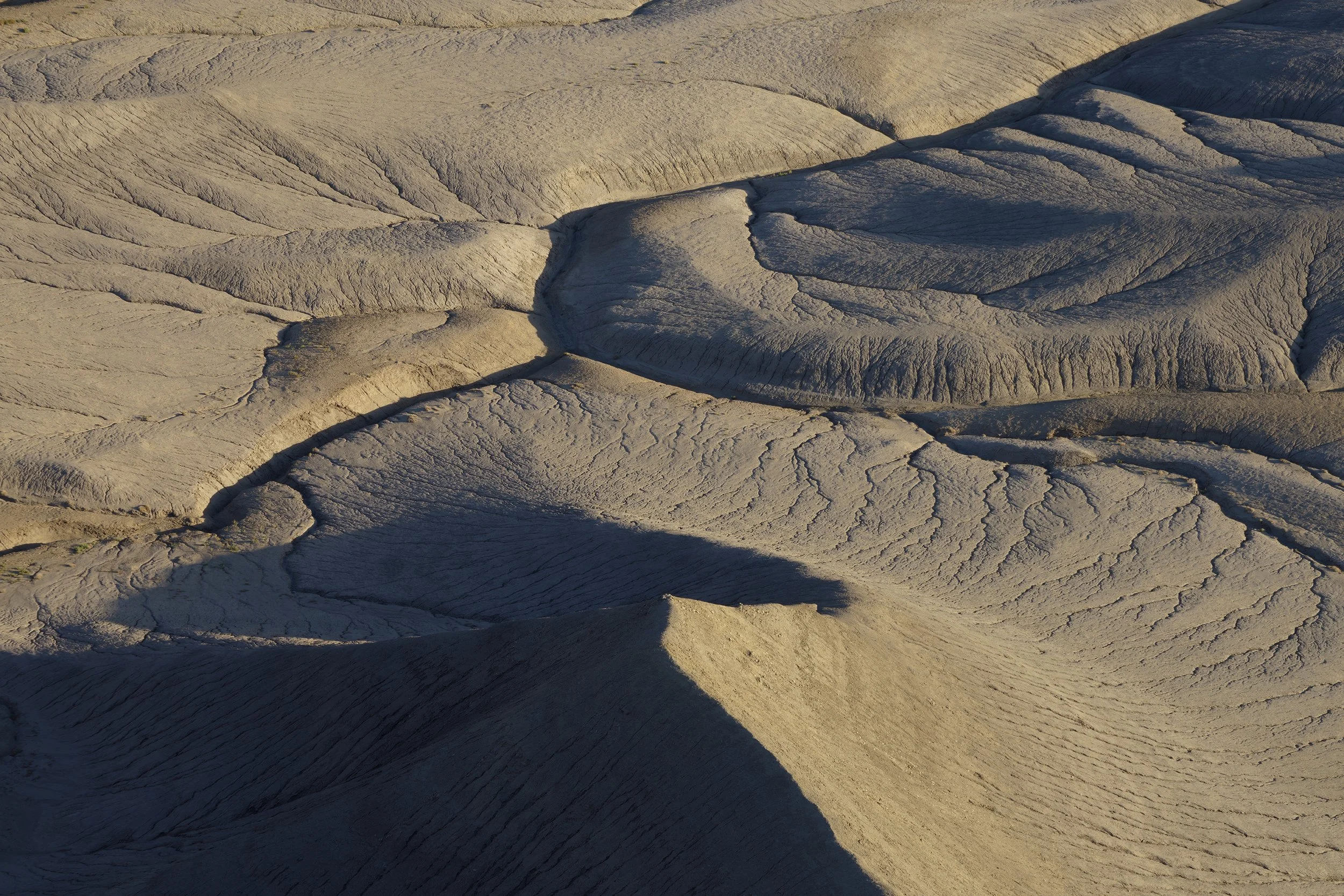Close-up aerial view of a glacial landscape showing textured and cracked ice formations with shadows cast on the surface.