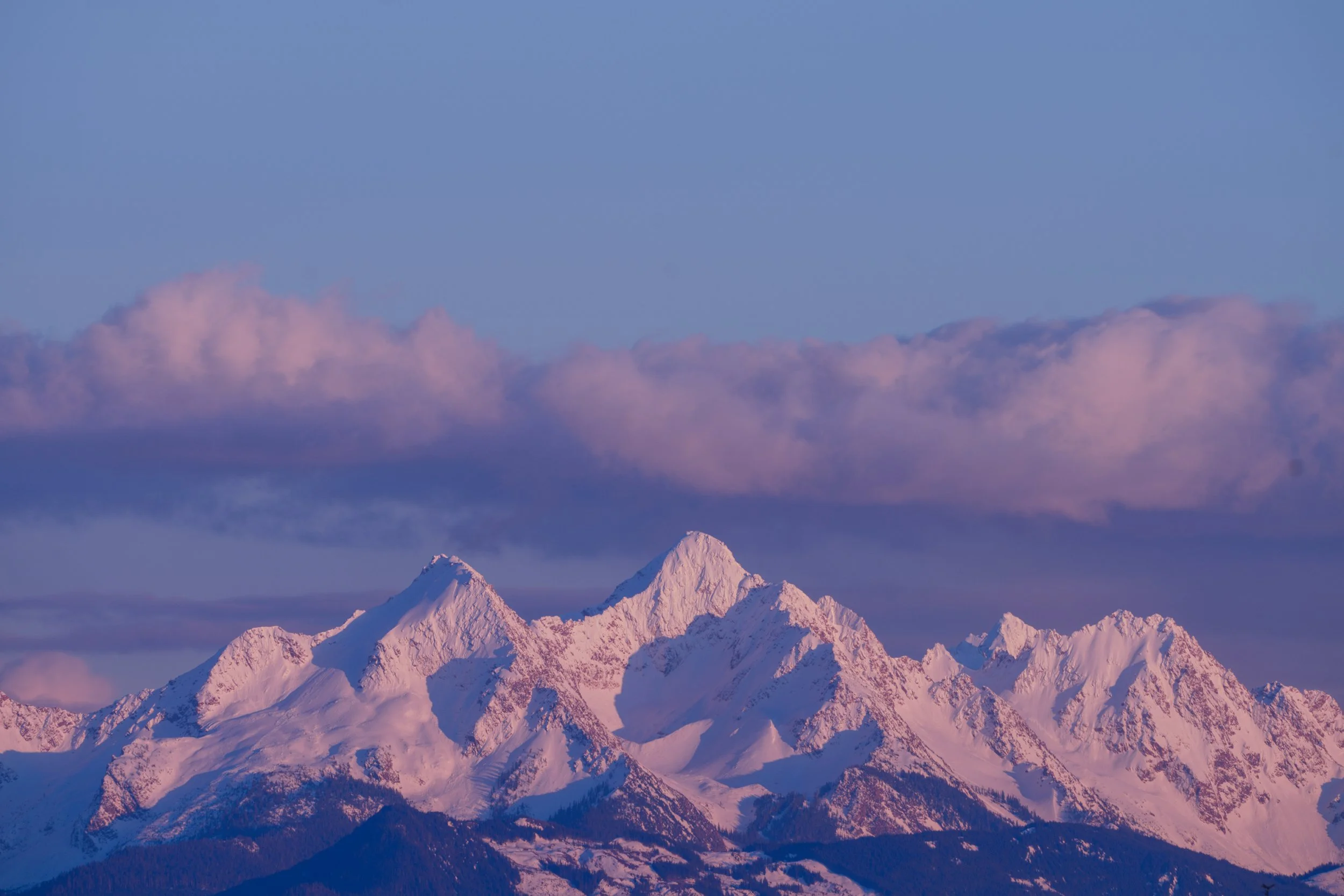 Snow-covered mountain peaks under a sky with pink and purple clouds.