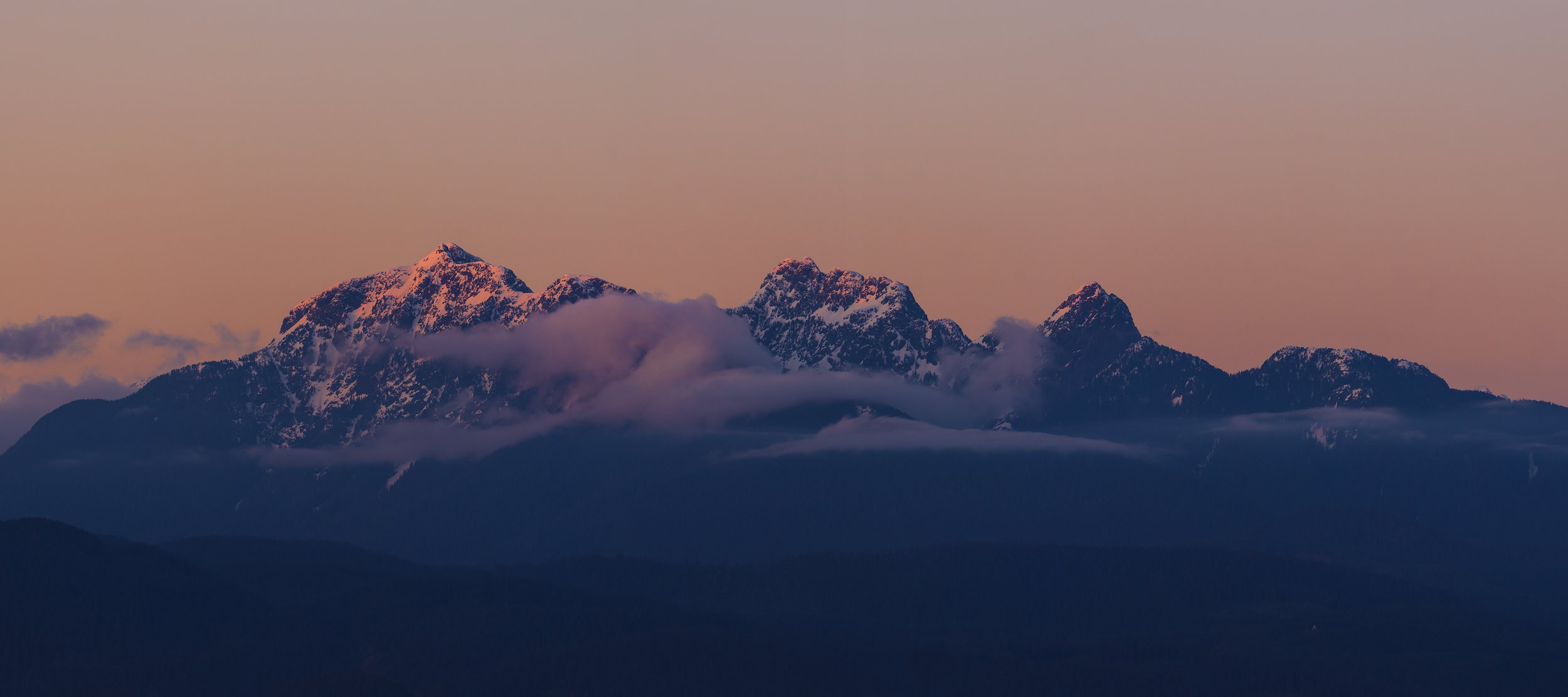 Snow-capped mountains at sunset with clouds and a pinkish sky.