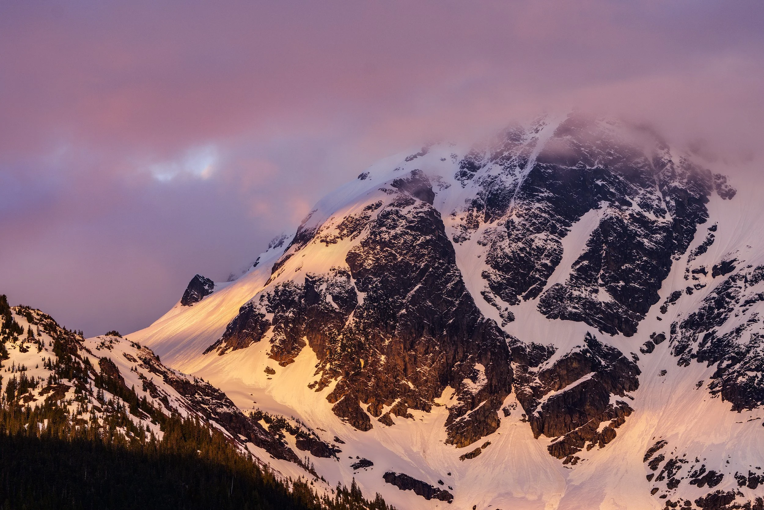 Snow-covered mountain peak at sunset with pink and purple sky.