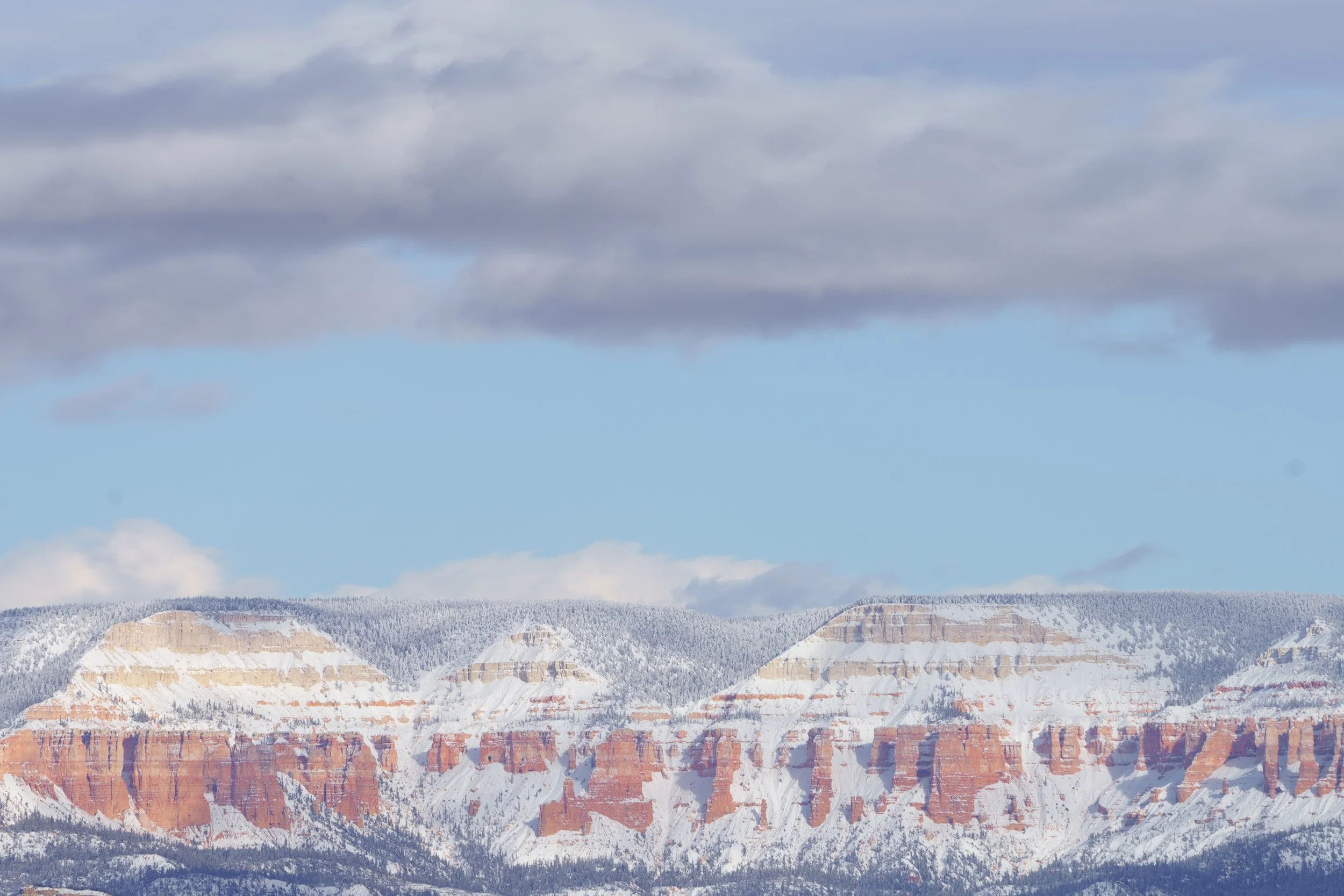 A scenic view of the Grand Canyon with snow-covered layers, under a cloudy sky.