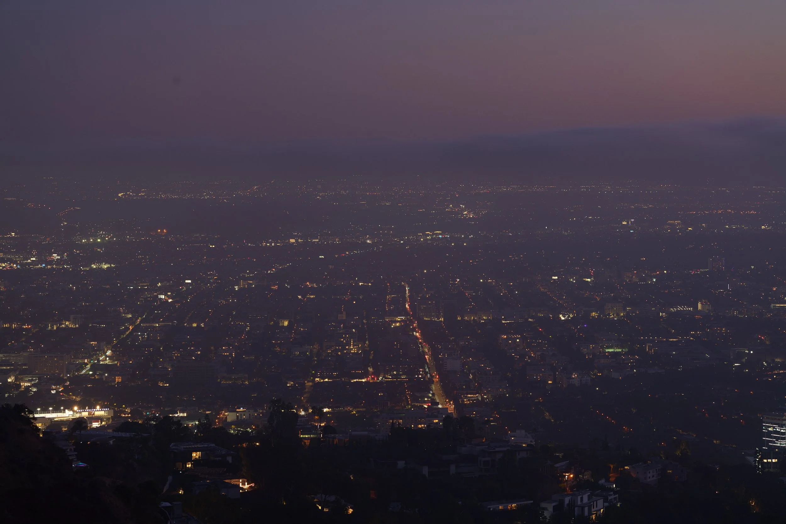 Nighttime cityscape with illuminated streets and buildings, sky transitioning from dusk to night.