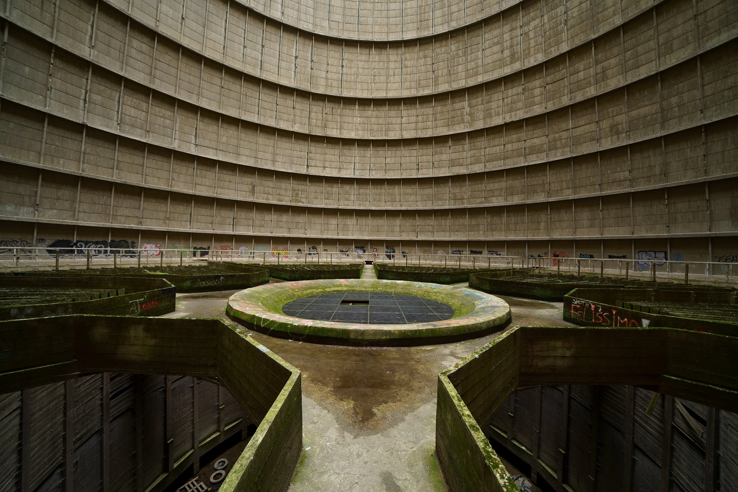 Inside an abandoned, large circular concrete water reservoir with graffiti and moss on the walls and mossy, empty flower beds on the floor.