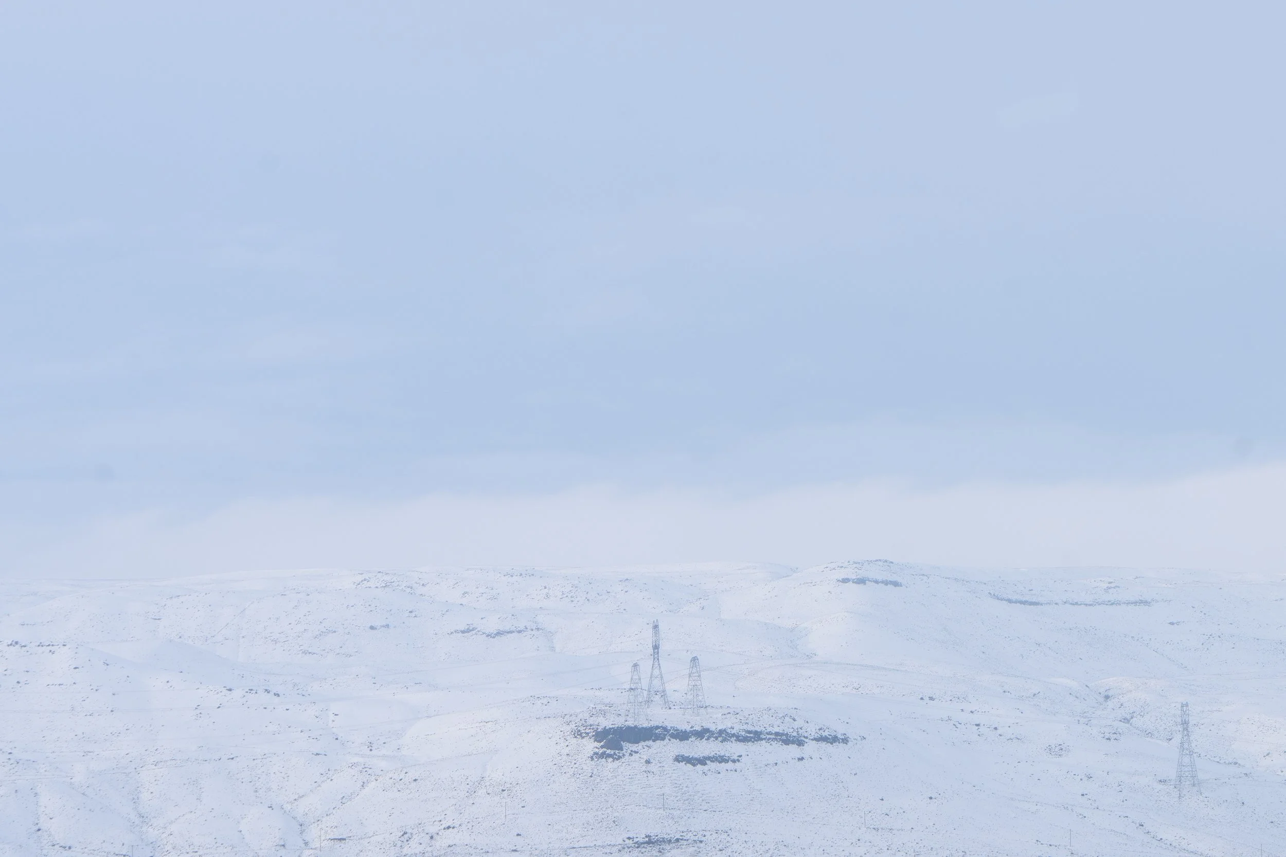 Snow-covered landscape with power lines and transmission towers under a cloudy sky.