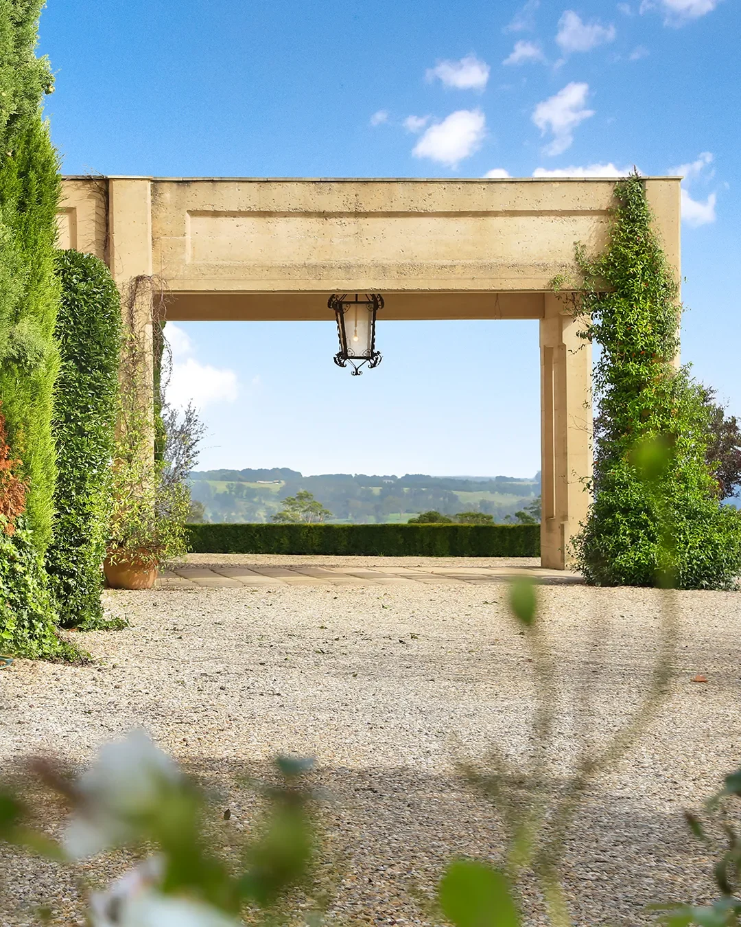 Open stone archway with greenery on sides and a view of rolling hills in the background.