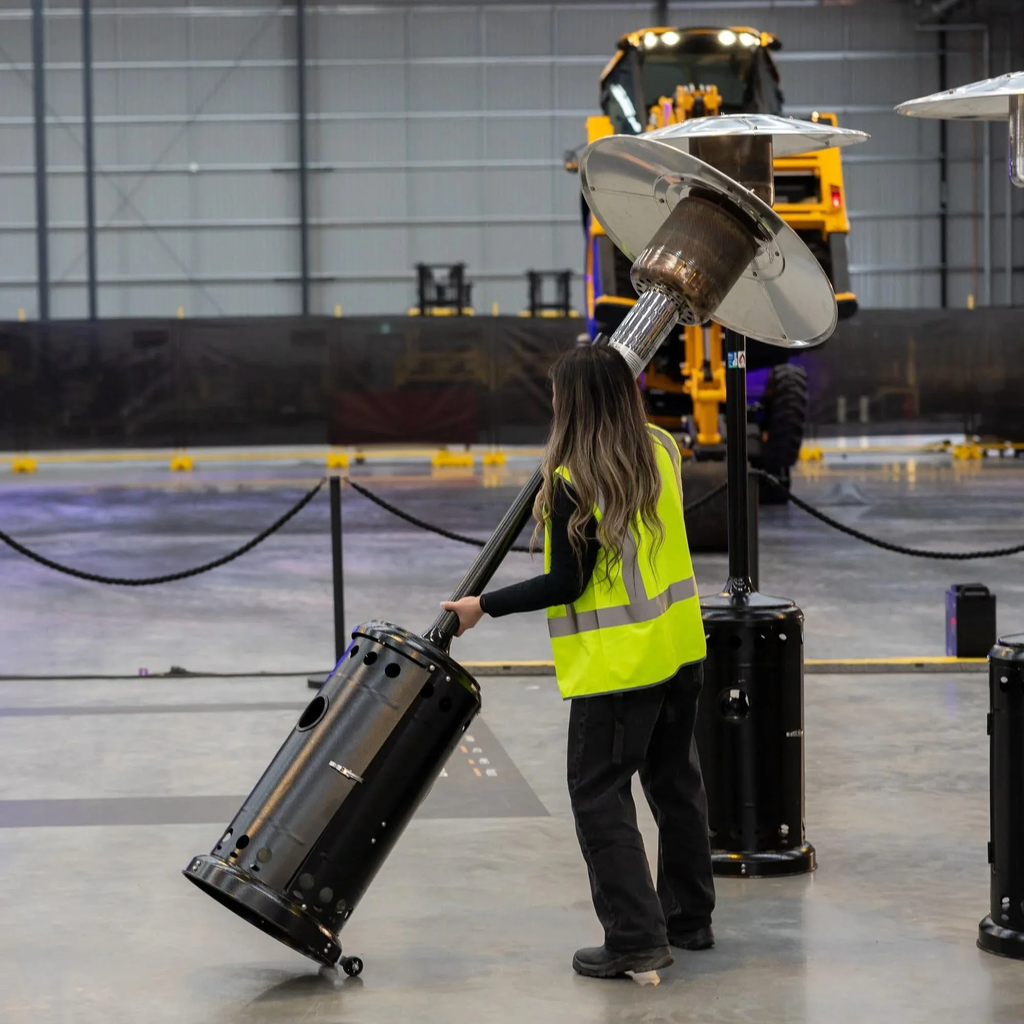 Event production team member in a high-visibility vest working with equipment inside a large industrial warehouse.