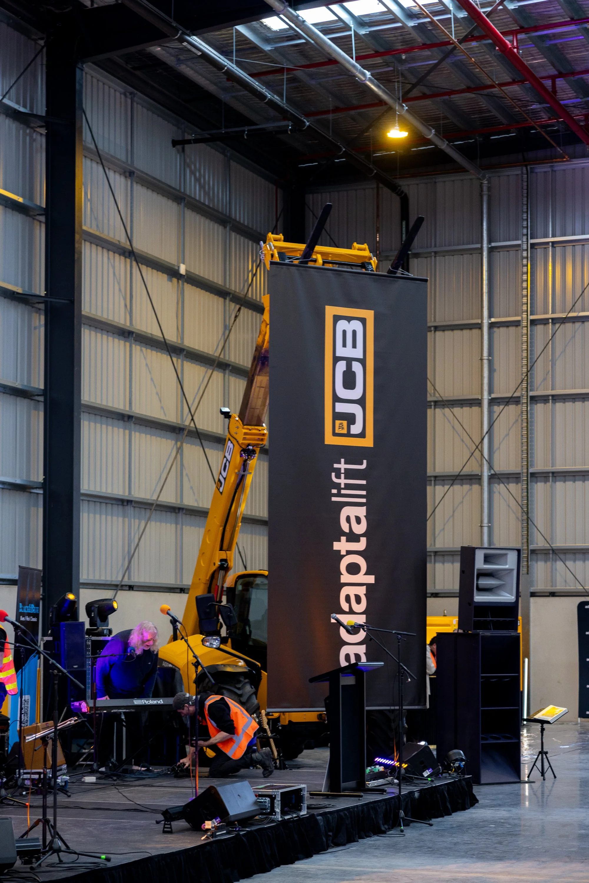 Musicians setting up equipment on stage at an indoor event with a large black banner displaying the words 'apartment lift' and a yellow crane in the background.