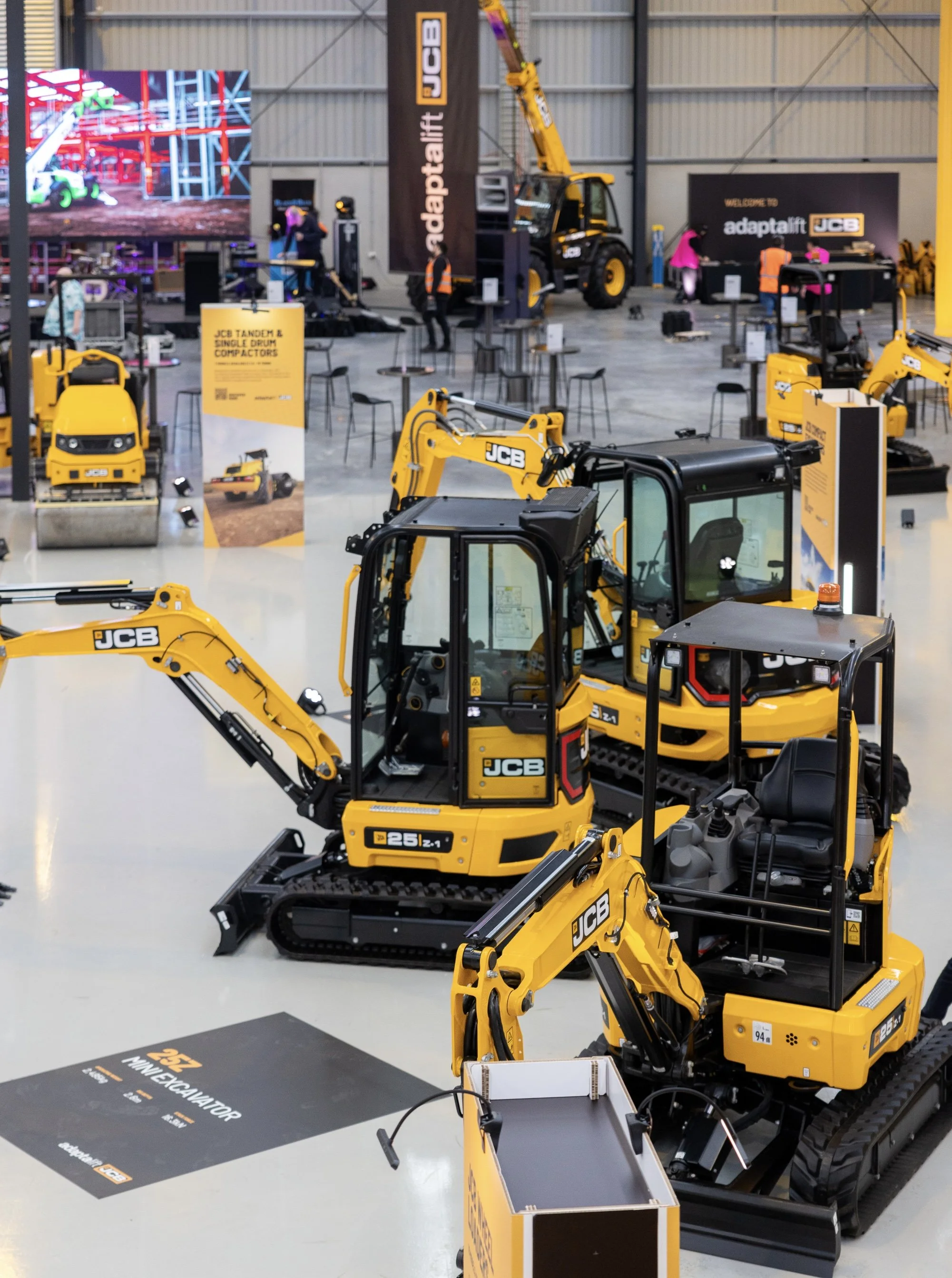 Display of JCB construction equipment including mini excavators with yellow and black color scheme at a trade show or exhibition.