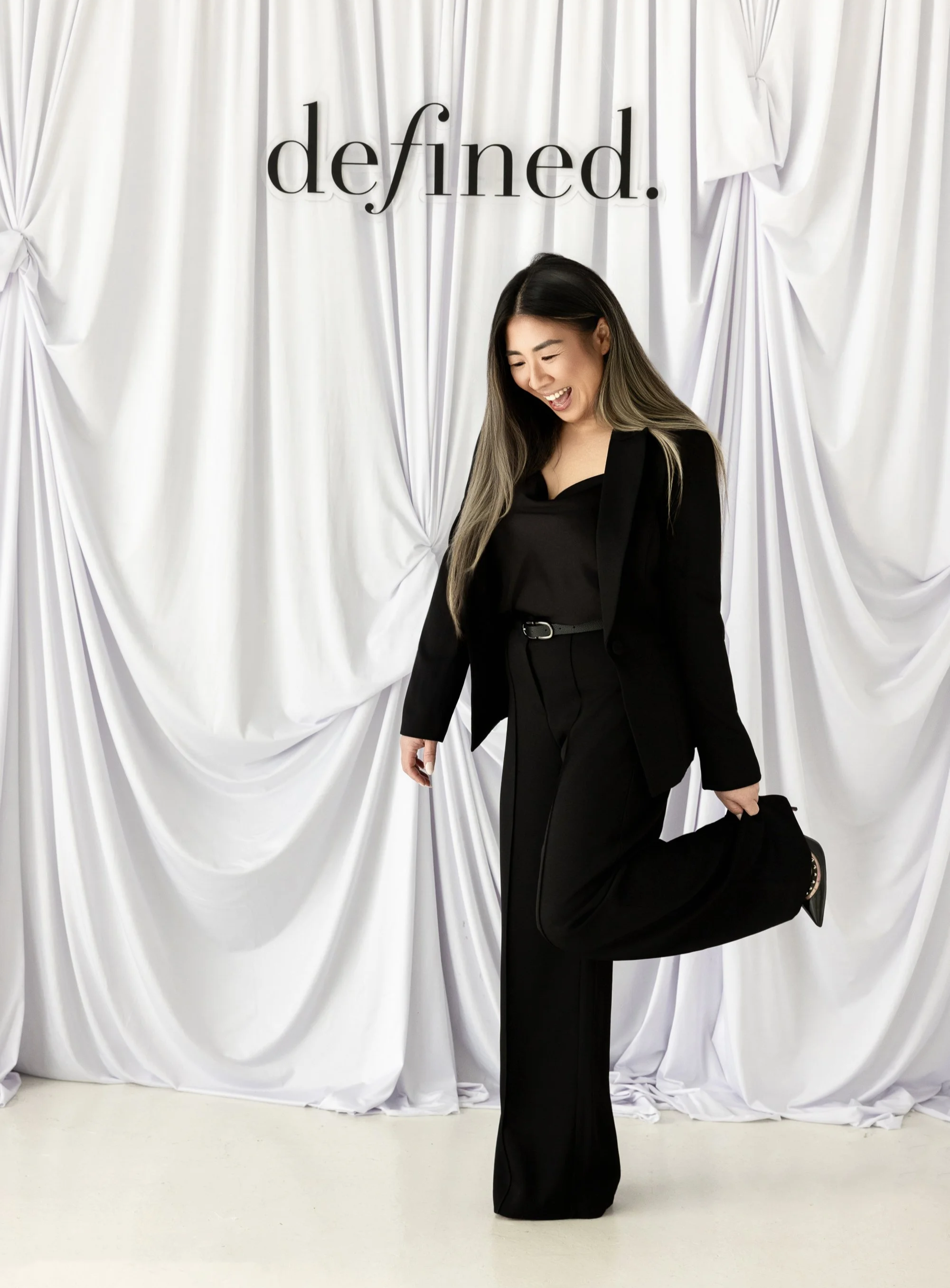 Behind the scenes at Defined, featuring the founder in an all-black outfit against an ivory draped backdrop with Defined. branding.
