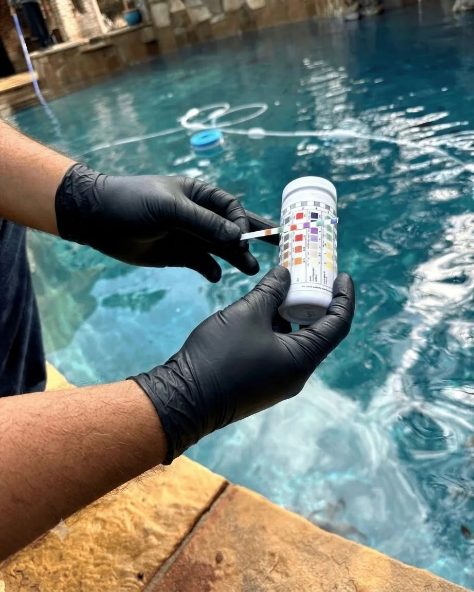 A person wearing black gloves holding a jar with a color test to check pool water, outdoors by a swimming pool.