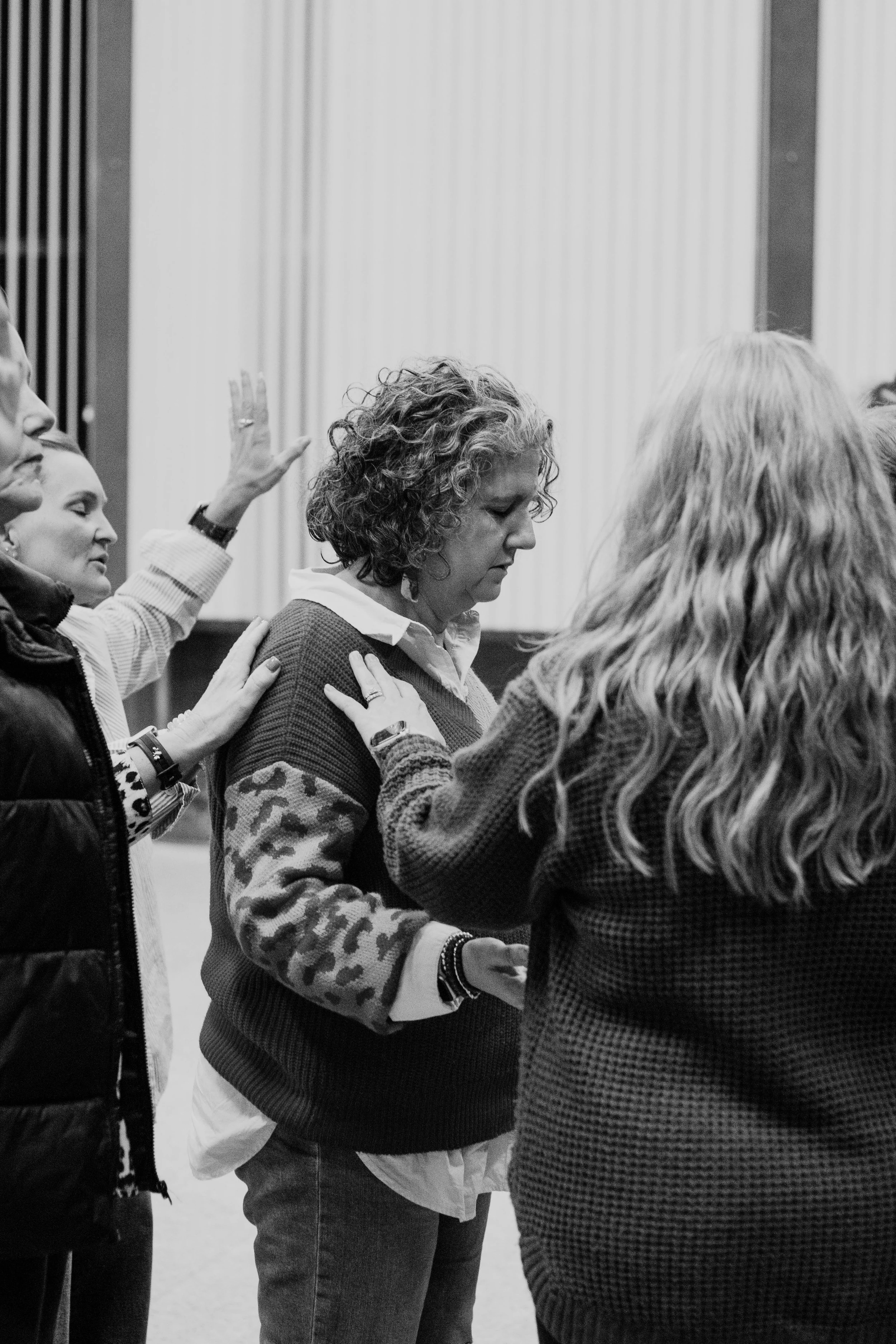 People praying in a church or religious gathering, with their eyes closed and hands on each other's shoulders.