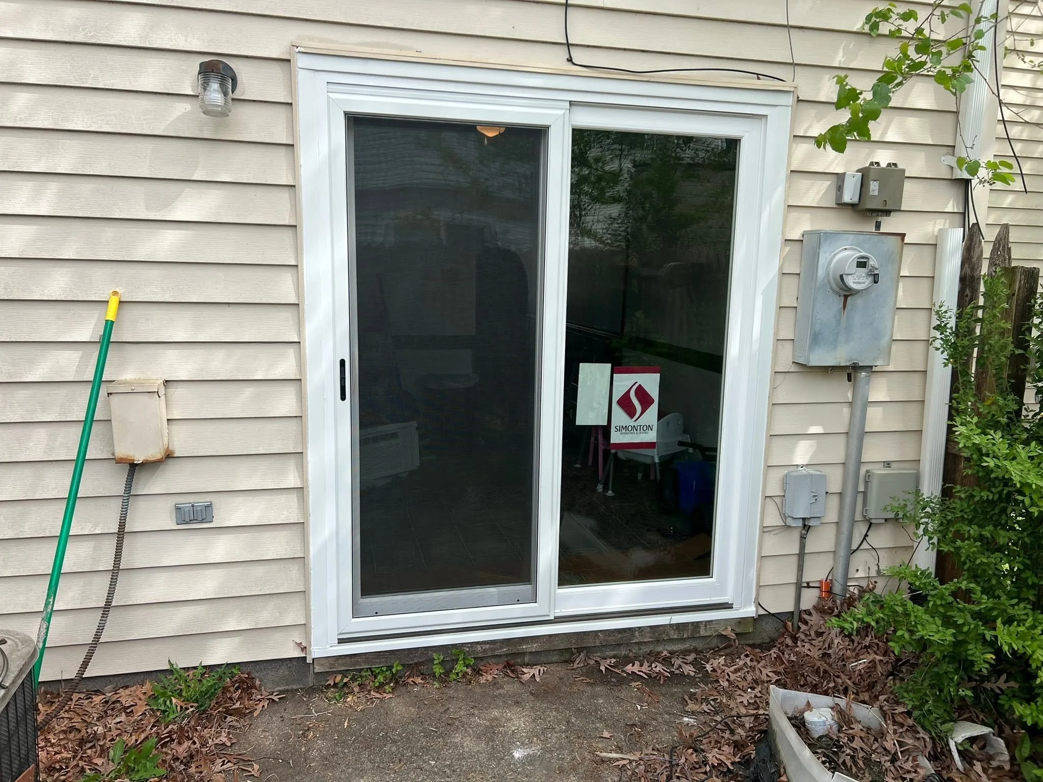 Image of a sliding glass door on a beige house with outdoor appliances and plants nearby.