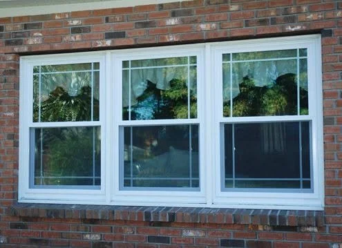 A large house window with three sections, reflecting trees and the sky outside.