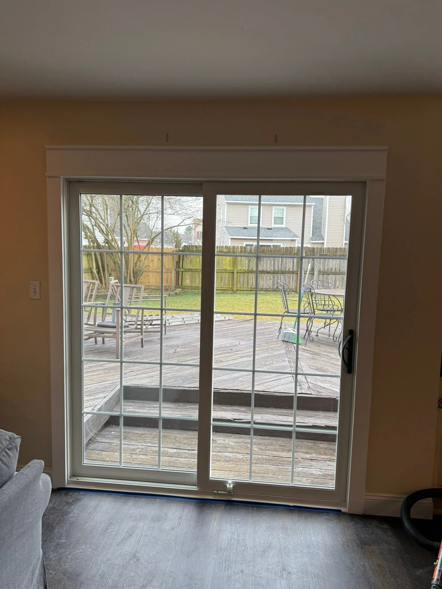 View through sliding glass door onto a wooden deck with outdoor furniture and a backyard enclosed by a wooden fence. Neighboring houses are visible in the background.