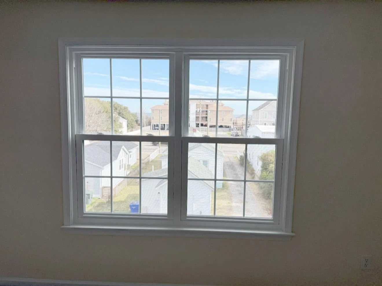 Photo of a double-paned window with white trim, showing a view of houses, trees, and a blue sky outside.