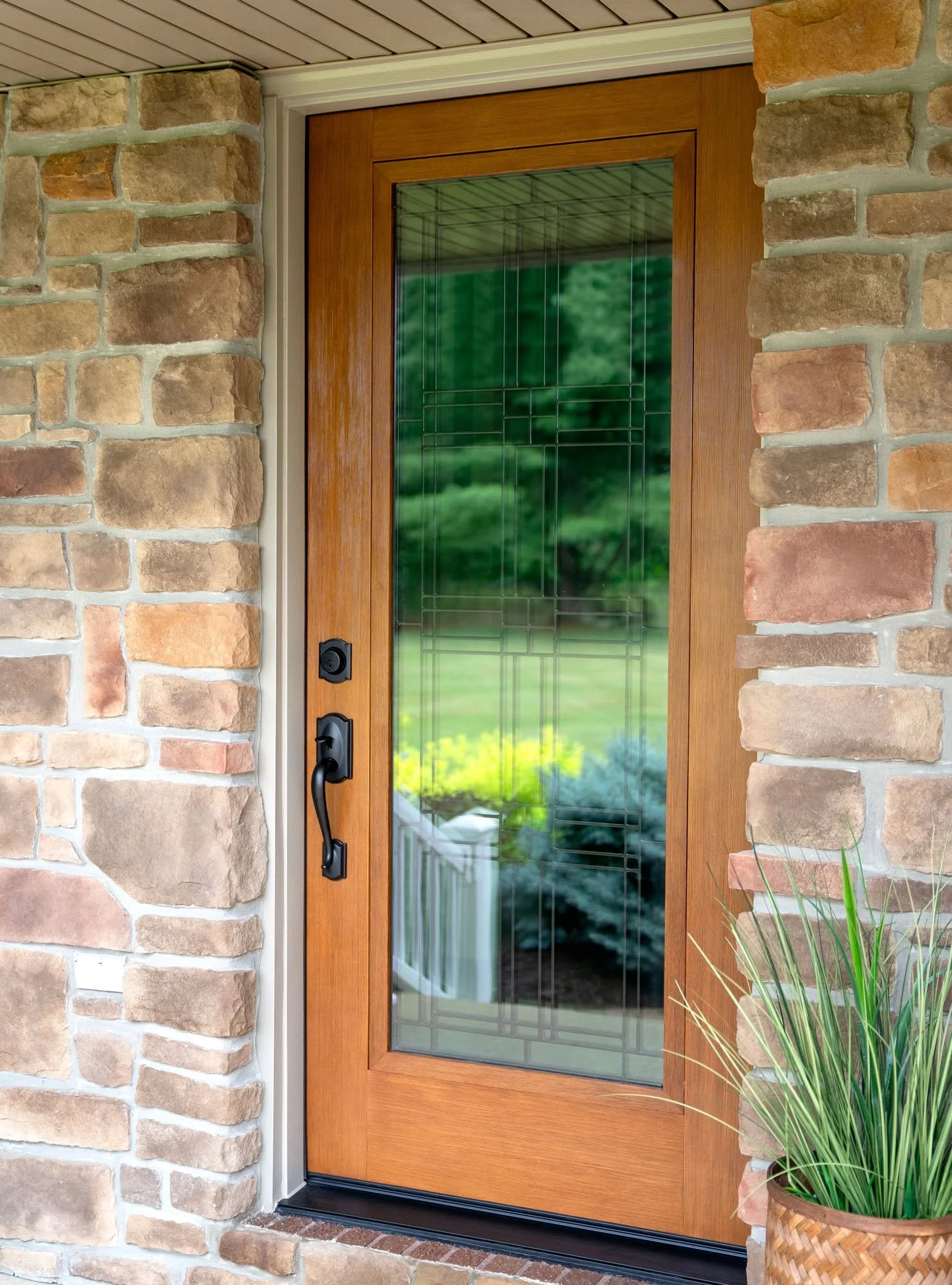 Front door with wood frame and glass panel, brick siding, and a potted plant nearby.