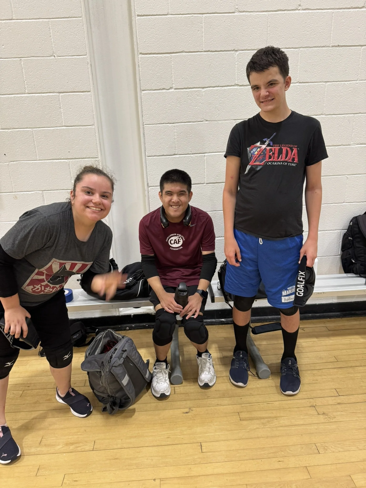 Goalball player playing a game at a practice at the Mission Valley YMCA. He's crouched and rolling the ball to the other side of the court