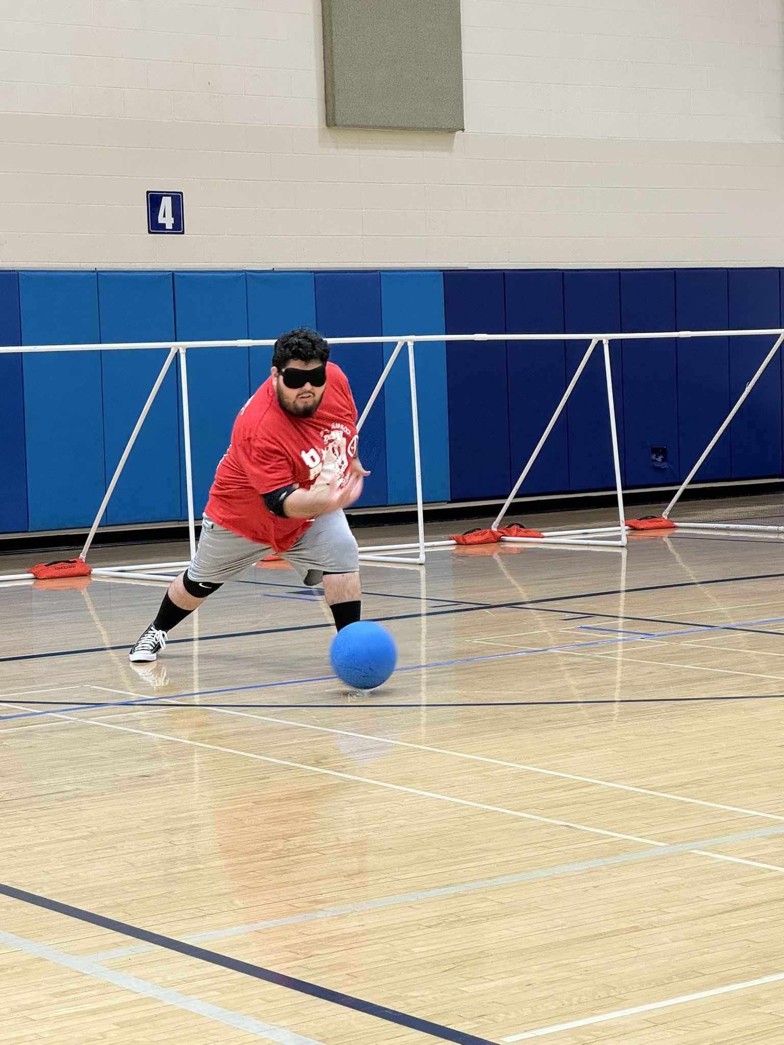 Angel wearing a red jersey throwing a goalball during a practice game.