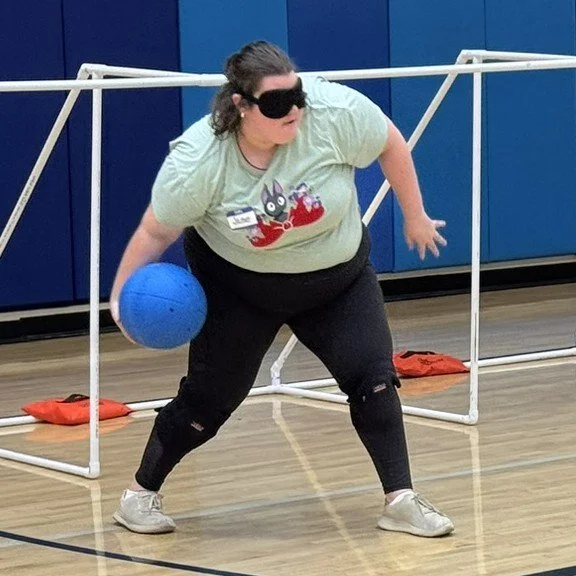 Photo of Jase, wearing a green shirt, throwing a goalball during a practice game.