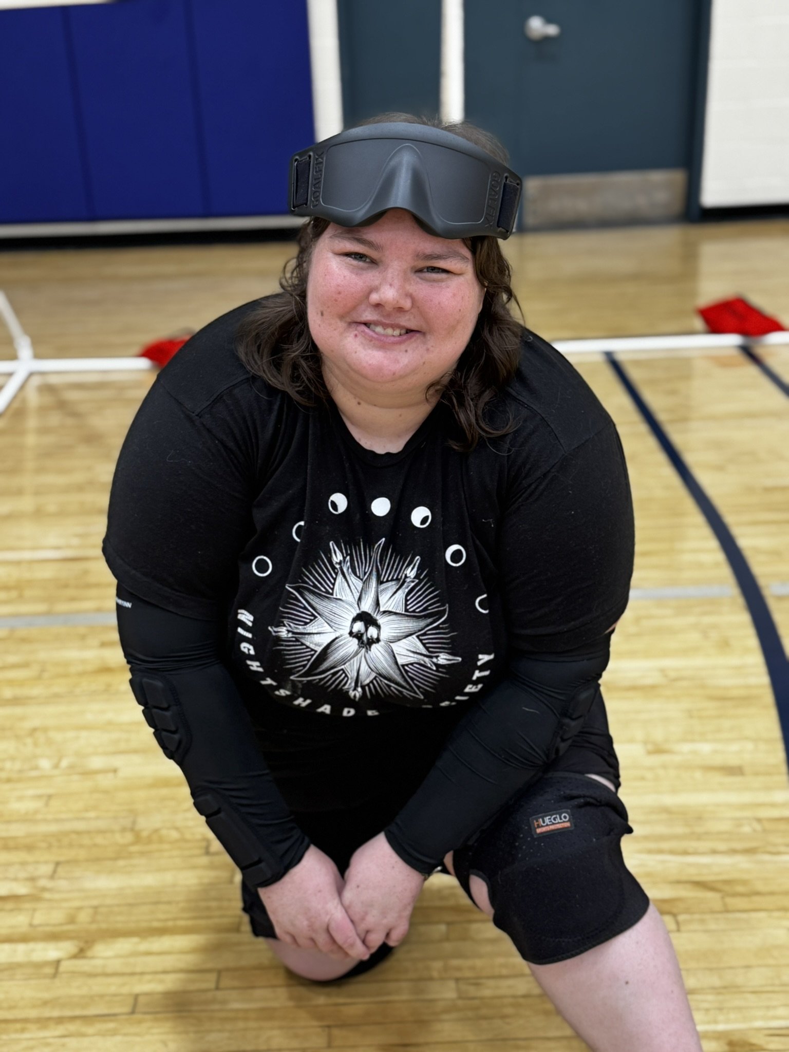 Photo of Jase posing in front of the goalball goals with her eyeshades on her forehead and a nice smile.